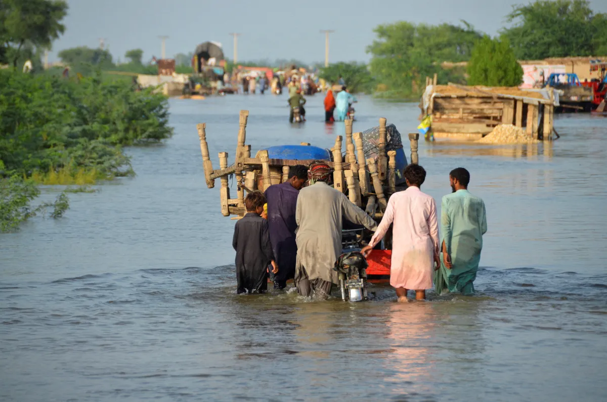 Men walk along a flooded road with their belongings, following rains and floods during the monsoon season in Sohbatpur, Pakistan