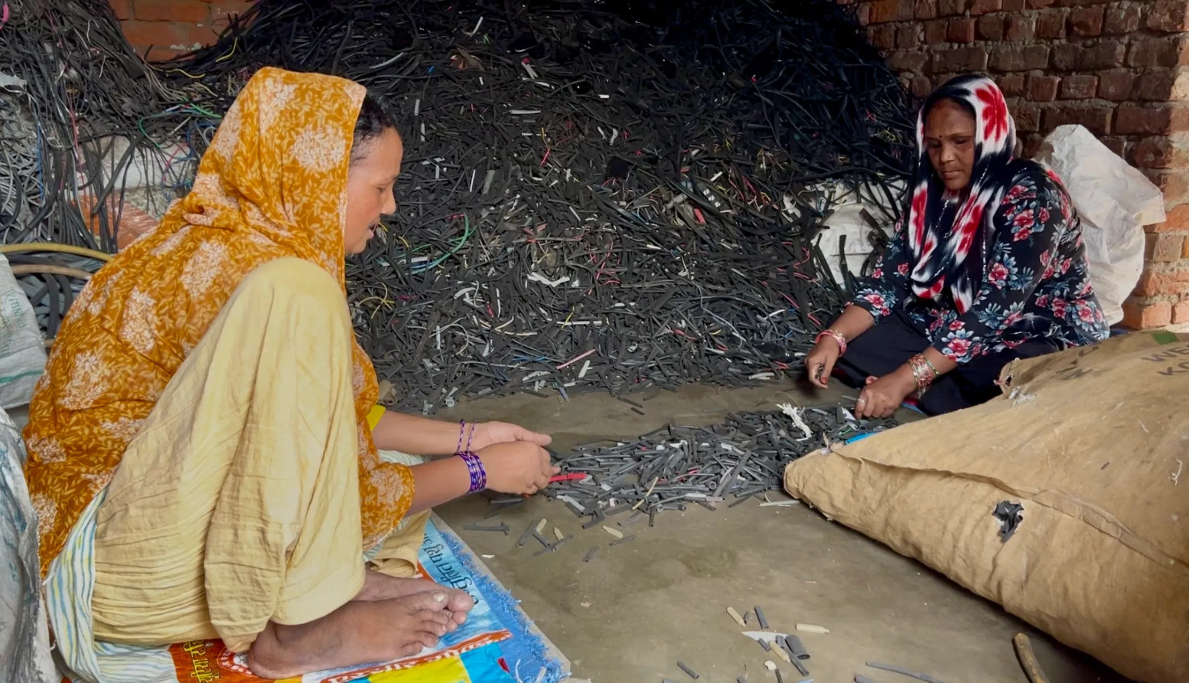 Women sorting through a heap of wire peels to segregate metals such as copper in Seelampur, Delhi. July 12, 2025. Thomson Reuters Foundation/Bhasker Tripathi