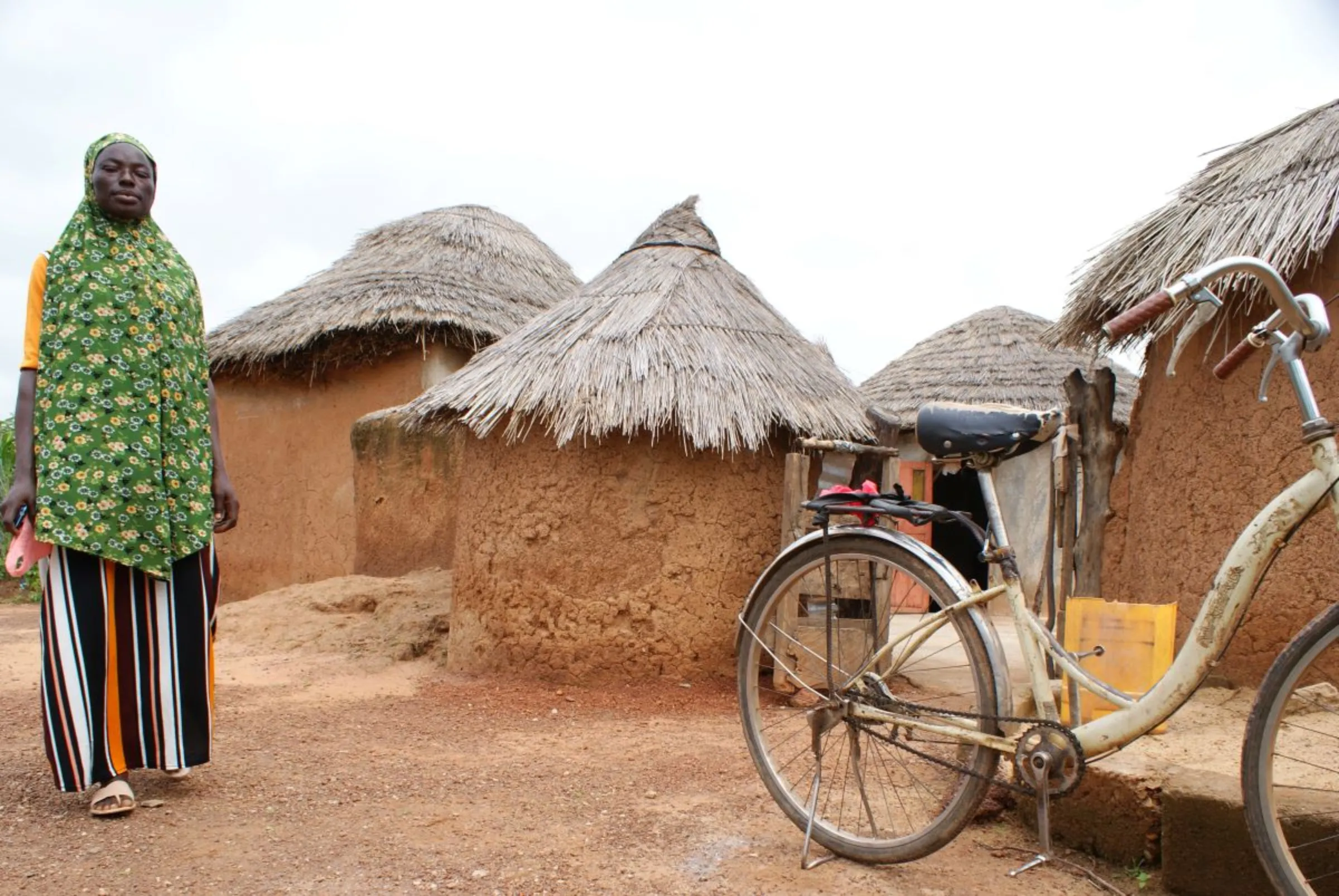 Adam Fuseina stands near the family bicycle at her home in Nafaring village,  northern Ghana, October 8, 2021. Thomson Reuters Foundation/Kagondu Njagi