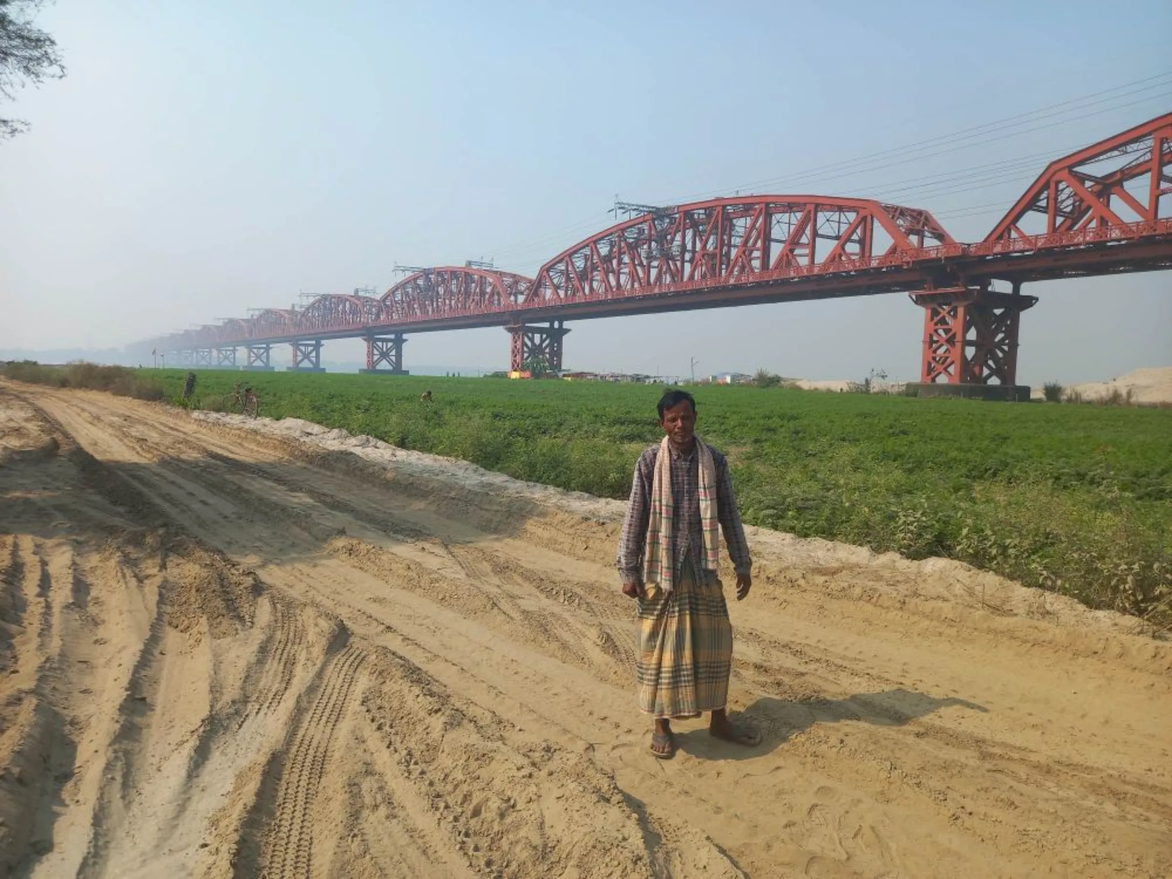 Rickshaw-puller Saidul Islam, 50, poses for a photo before the century-old Hardinge Bridge across the Padma River on whose bank the Rooppur plant is situated,  Bangladesh, 15 December 2022