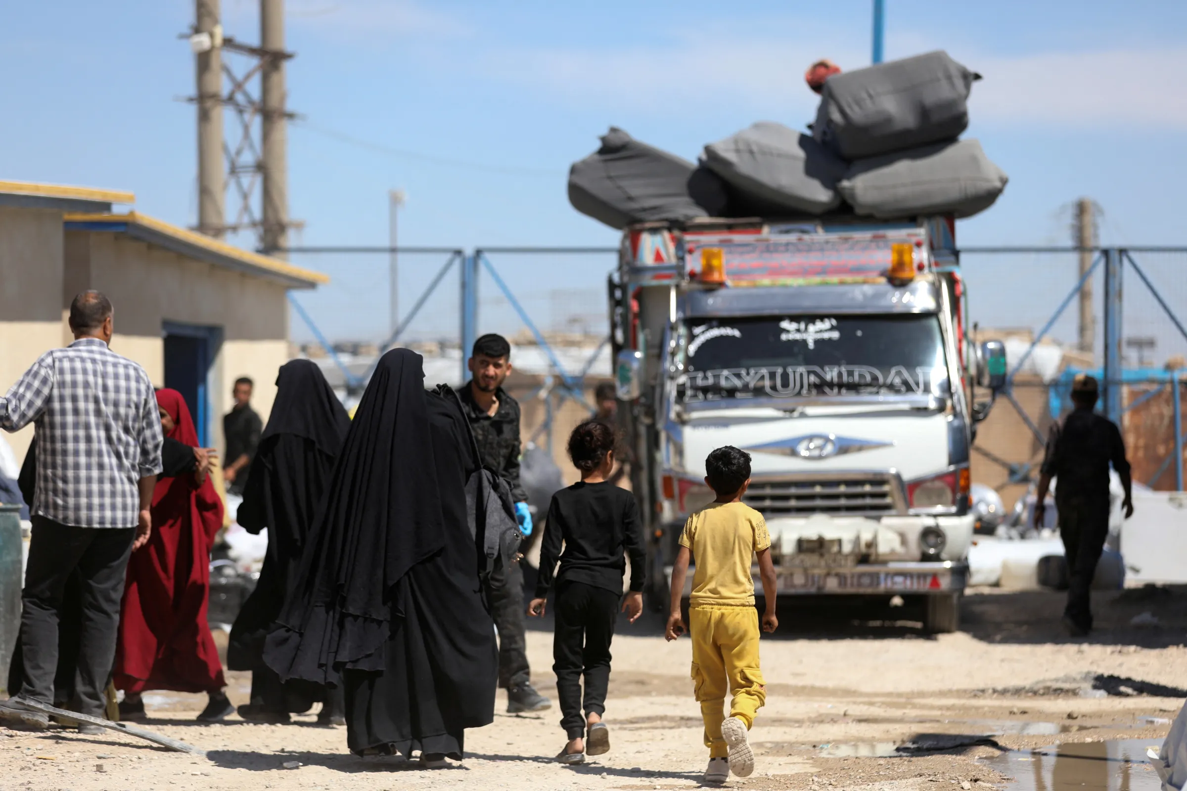 People walk by a vehicle loaded with belongings as they prepare to leave the al-Hol refugee camp to go back to their hometowns, in al-Hol, Syria, April 27, 2025. REUTERS/Orhan Qereman
