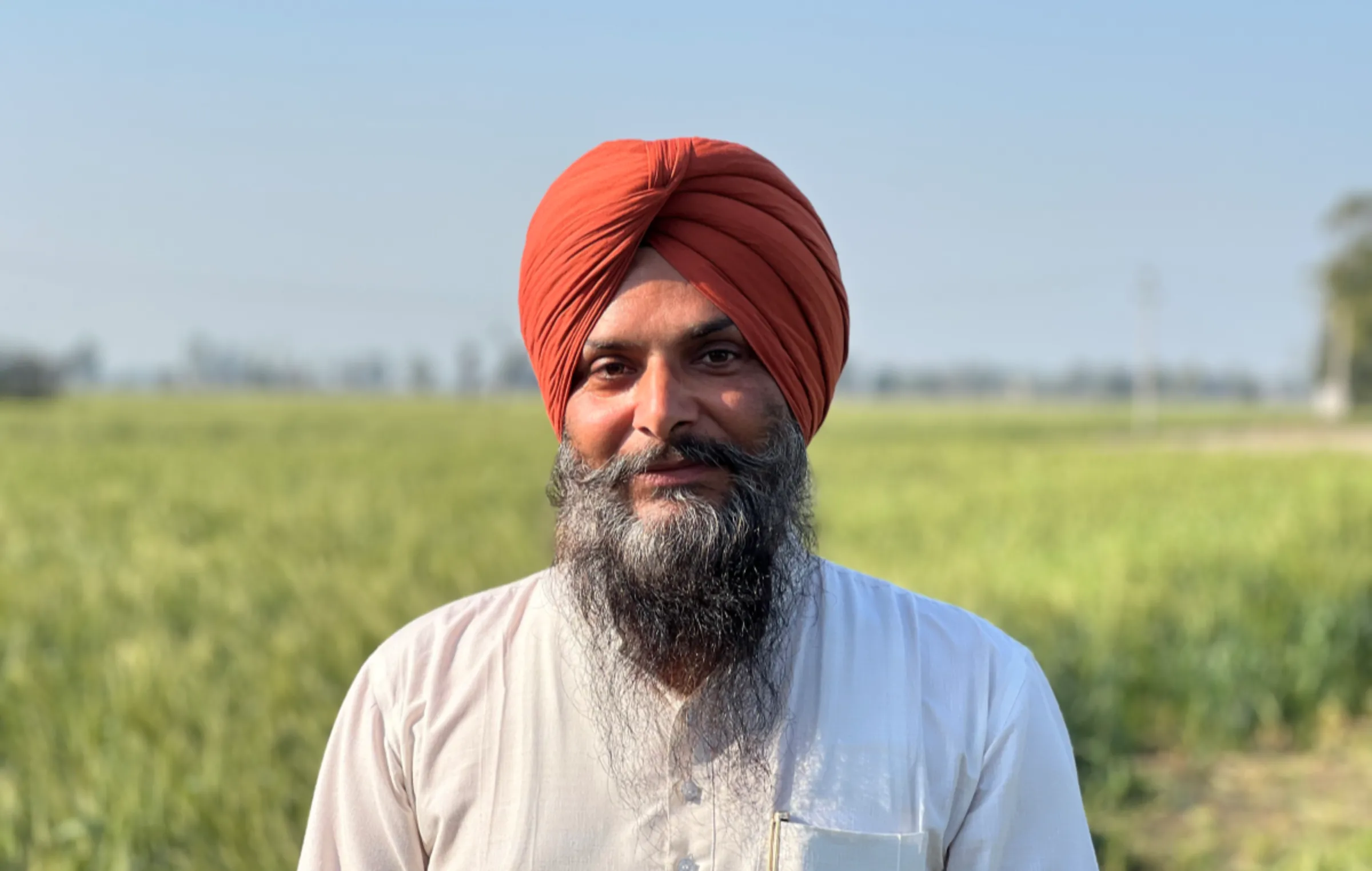 Small-scale seed dealer Palvinder Singh stands next to a field of wheat in Karnal, India, on March 11, 2024. Thomson Reuters Foundation/Bhasker Tripathi