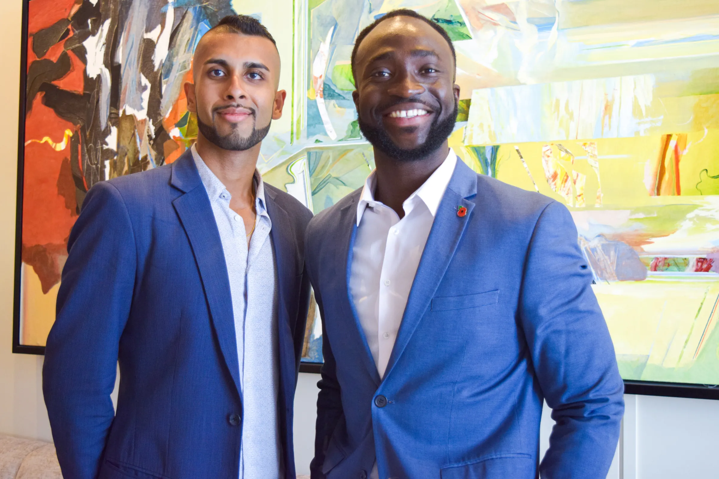 Two men are photographed in front of a coloured painting