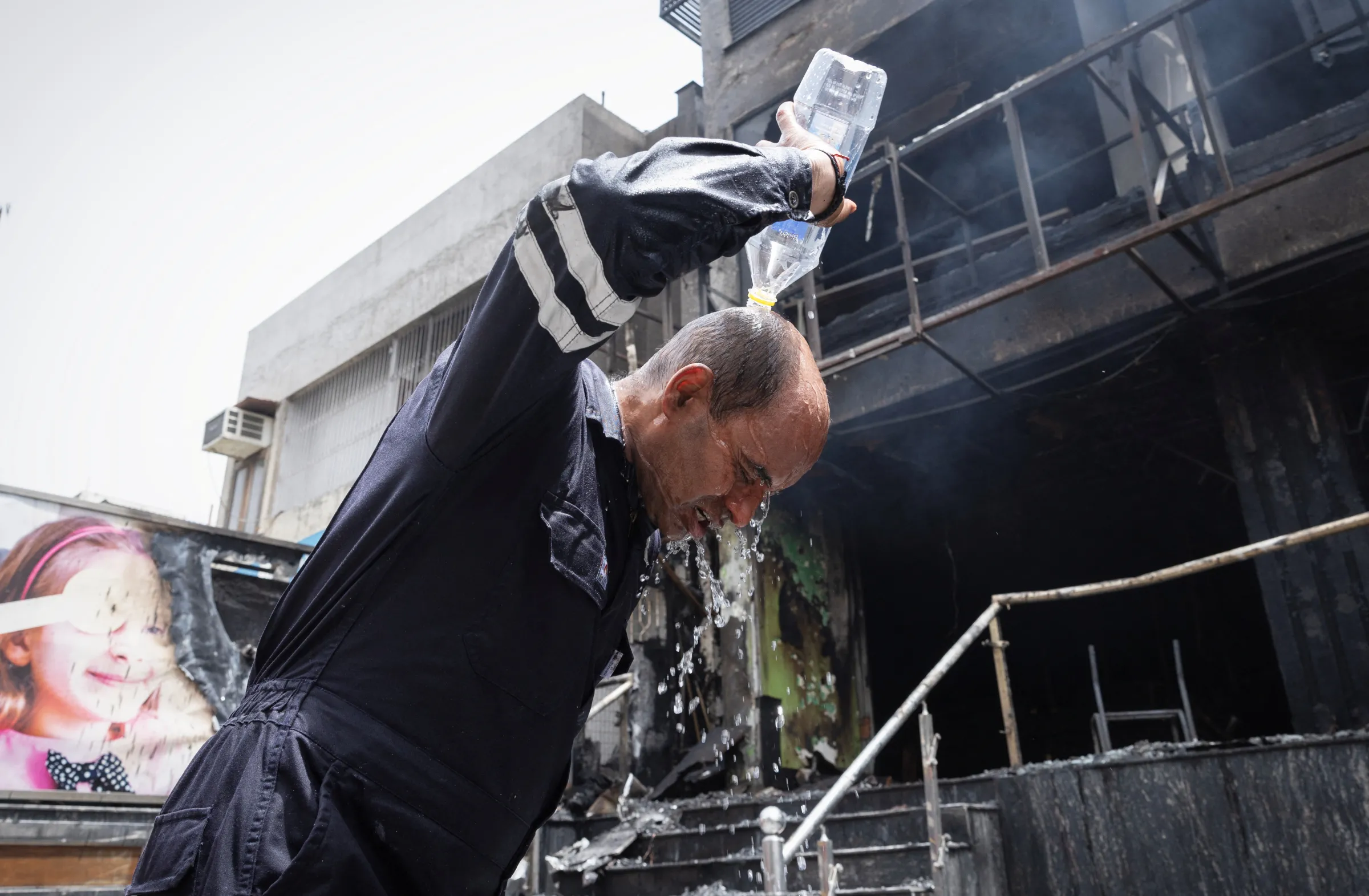 A firefighter, pours water on his head to cool himself down after coming out of a burning eye hospital in New Delhi, India, June 5, 2024. REUTERS/Adnan Abidi