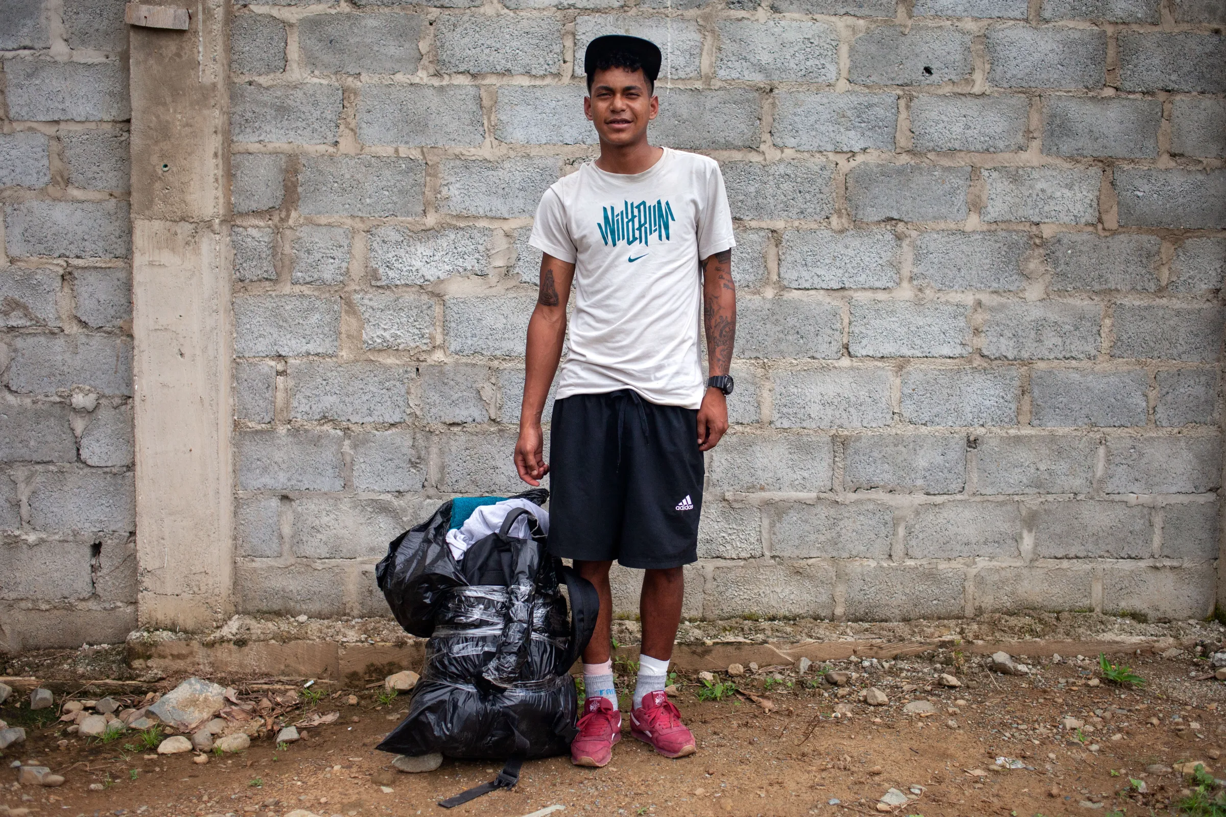 Wilbar, a 19-year-old Venezuelan migrant traveling with a group of Venezuelan families, at a camping site in the Colombian town of Capurganá, standing next to his backpack wrapped with plastic to protect it from the rain before starting the jungle trek through the Darién Gap. Capurganá, Colombia, July 27, 2022. Thomson Reuters Foundation/Fabio Cuttica