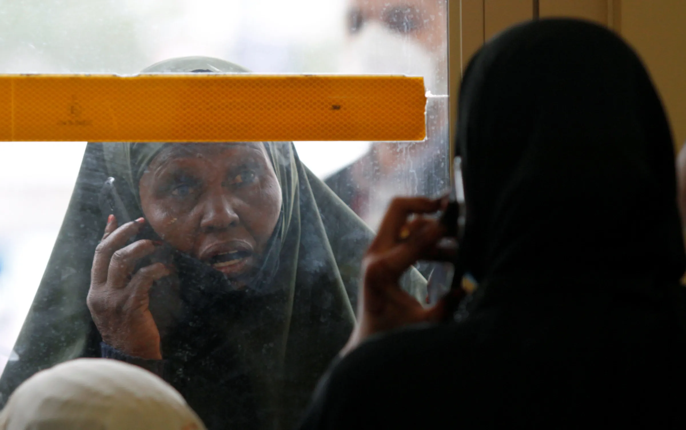 A relative outside the terminal and a passenger use mobile phones as they talk near a glass door at the Jomo Kenyatta international airport in Nairobi, Kenya August 1, 2020