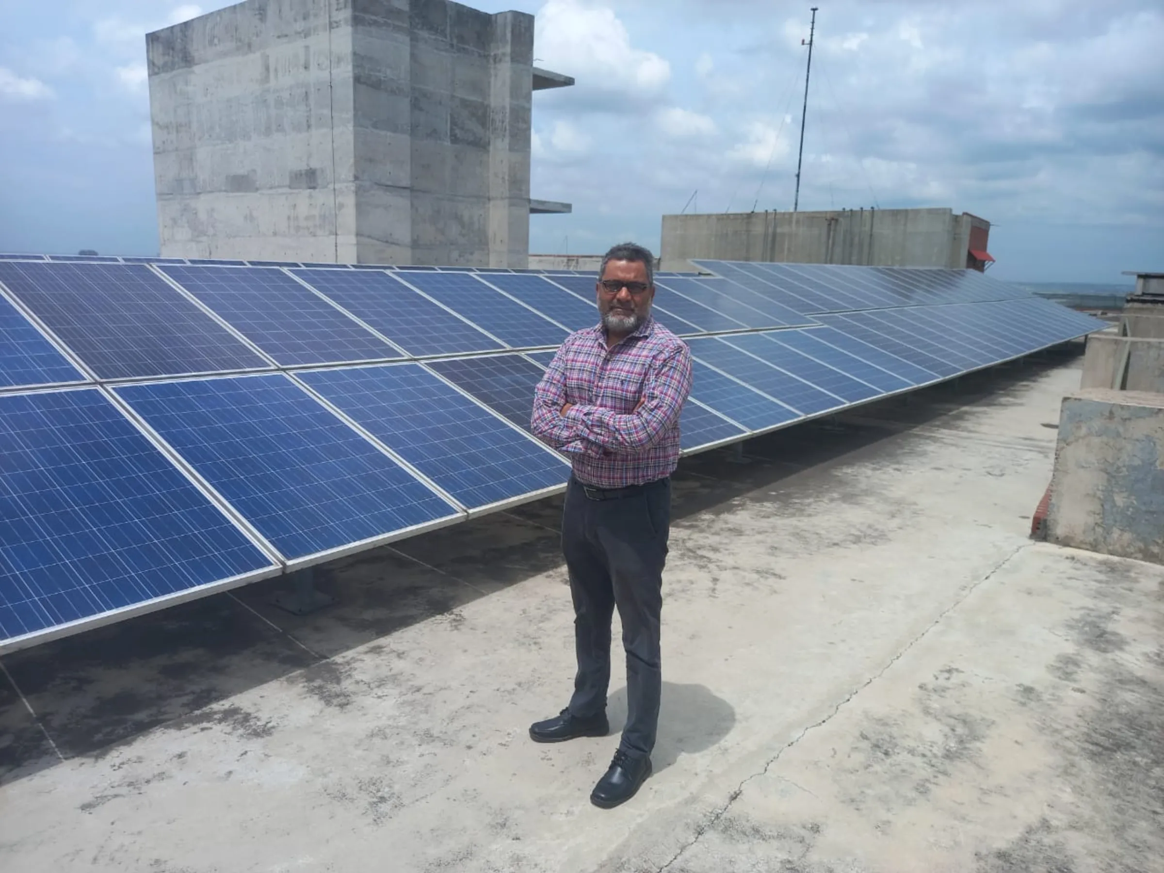 A man stands with his arms folded in front of solar panels on a rooftop