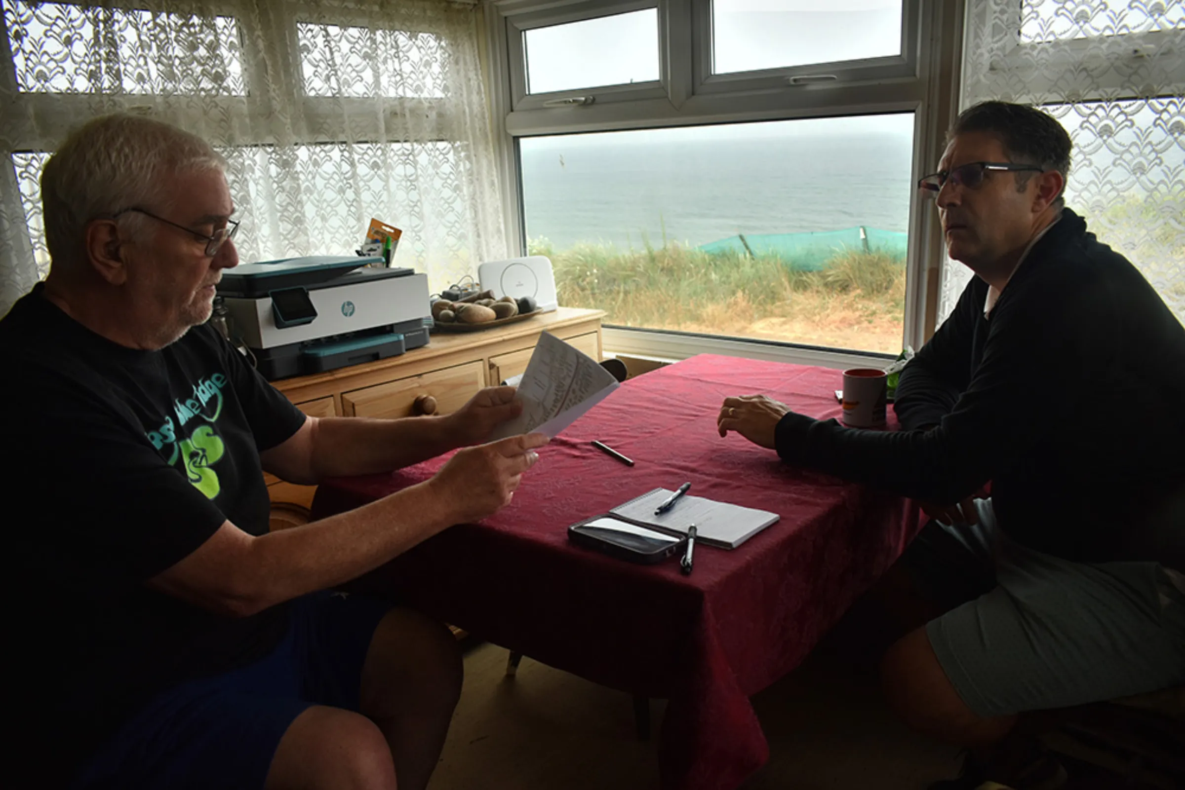 Kevin Jordan, left, and his neighbor Simon Measures discuss an old land registry diagram and the coastal erosion they’ve seen in front of their homes, Hemsby, England, June 20, 2023. Thomson Reuters Foundation/Rachel Parsons