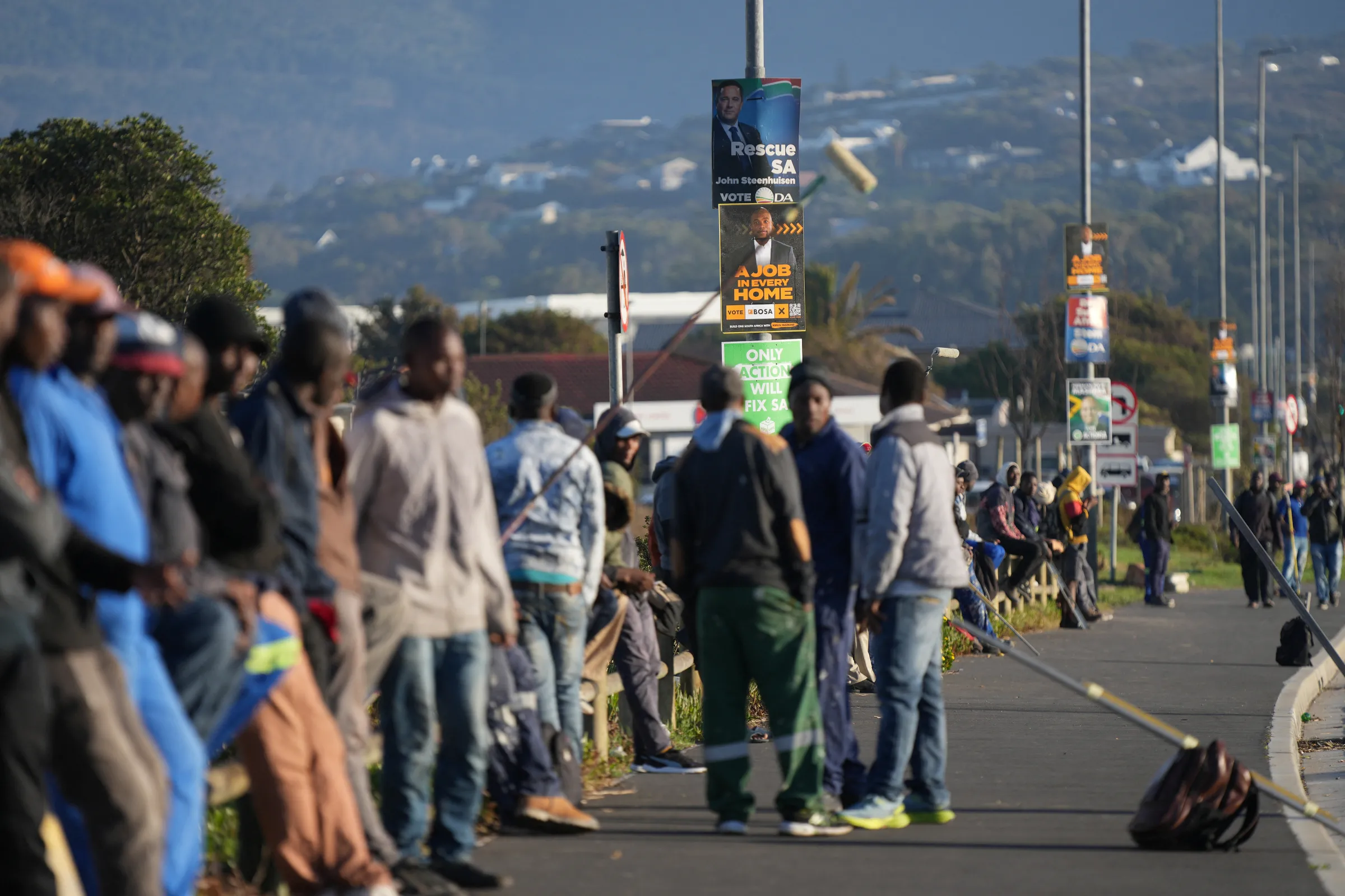 Unemployed job seekers line a street waiting for casual employment, as they sit beneath election campaign posters for the South African general elections which will be held on May 29, in Cape Town, South Africa, April 19, 2024. REUTERS/Nic Bothma
