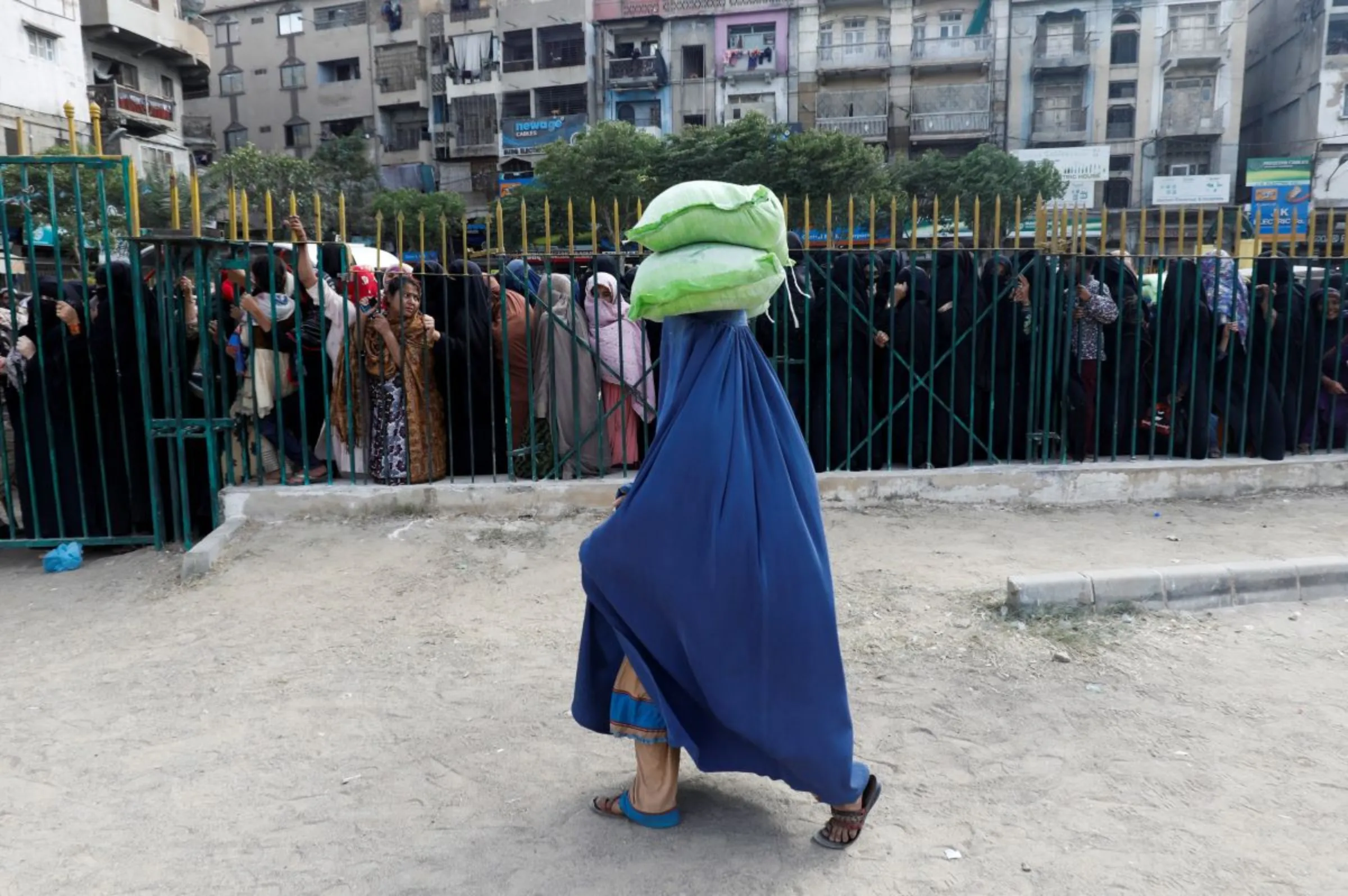 A woman walks with sacks of flour on her head, purchased from a truck at subsidised rates, while others stand in queue in Karachi, Pakistan January 11, 2023. REUTERS/Akhtar Soomro