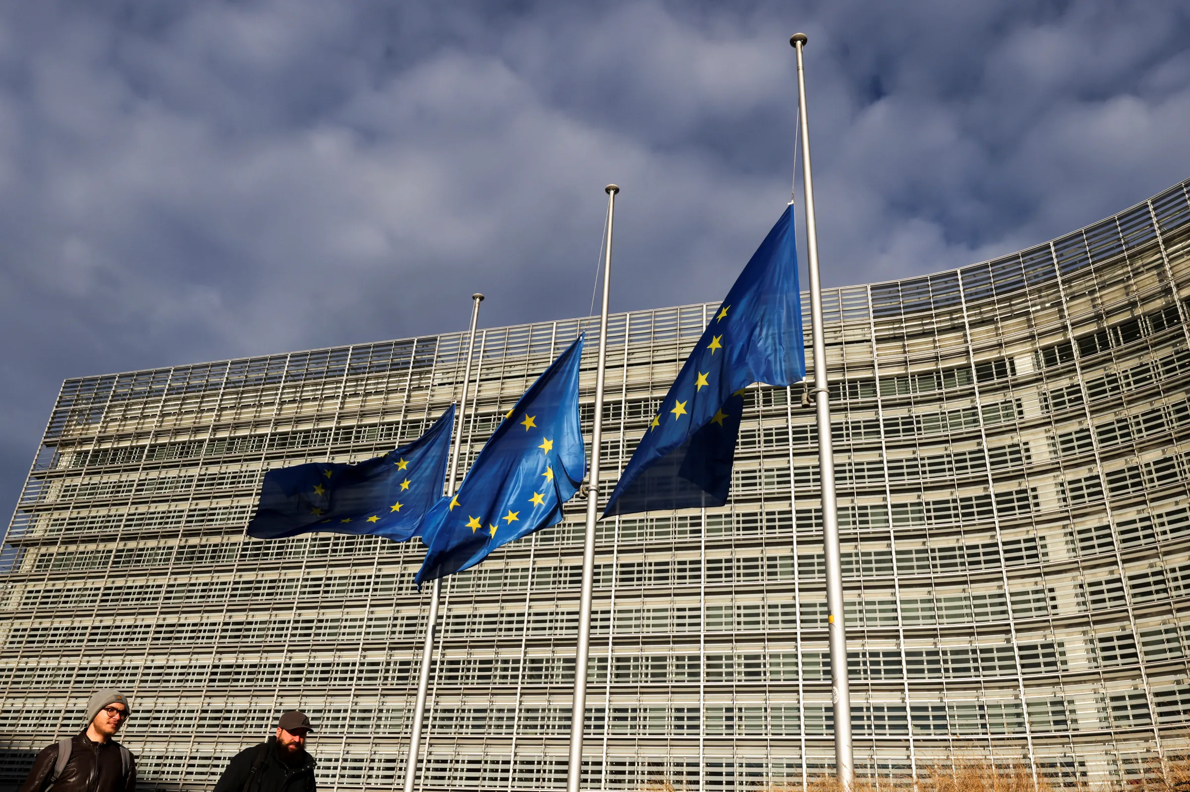 People walk past as European Union's flags flutter at half mast in memory of late European Parliament President David Sassoli, in front of European Commission building, in Brussels, Belgium January 11, 2022