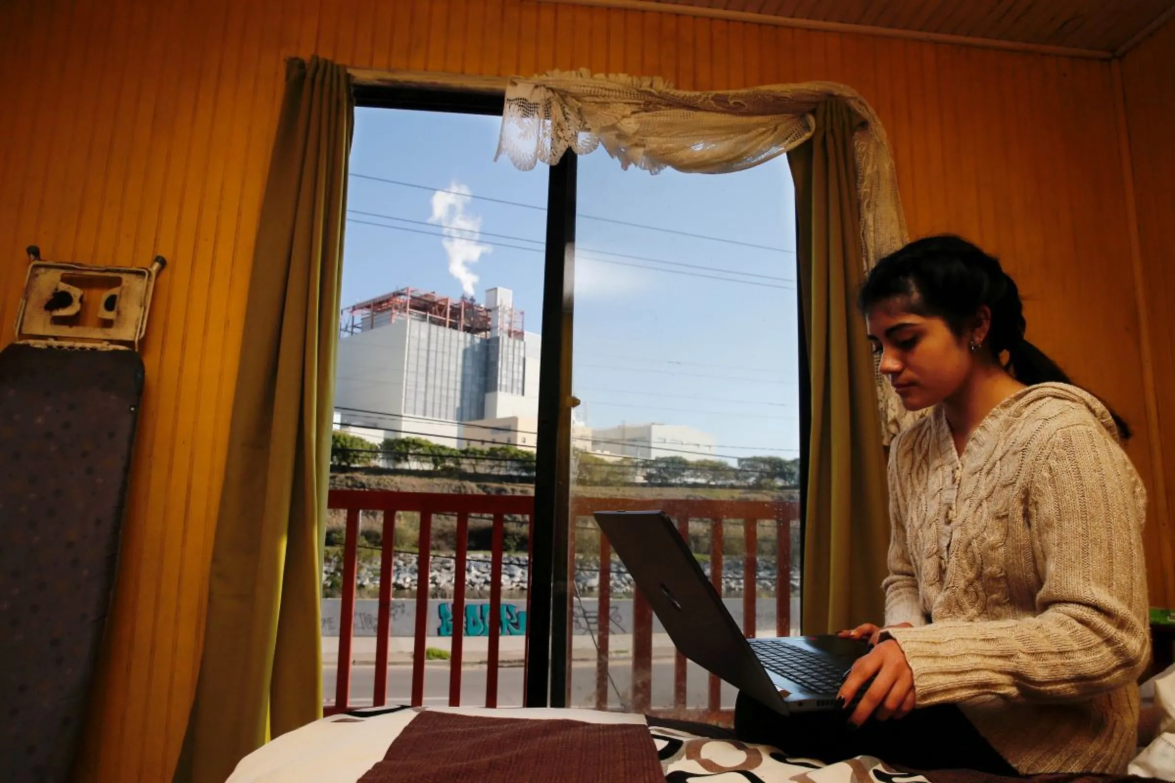 A girl works on her laptop inside of her house in front of the refinery of Puerto Ventanas in Ventanas, Chile September 1, 2018