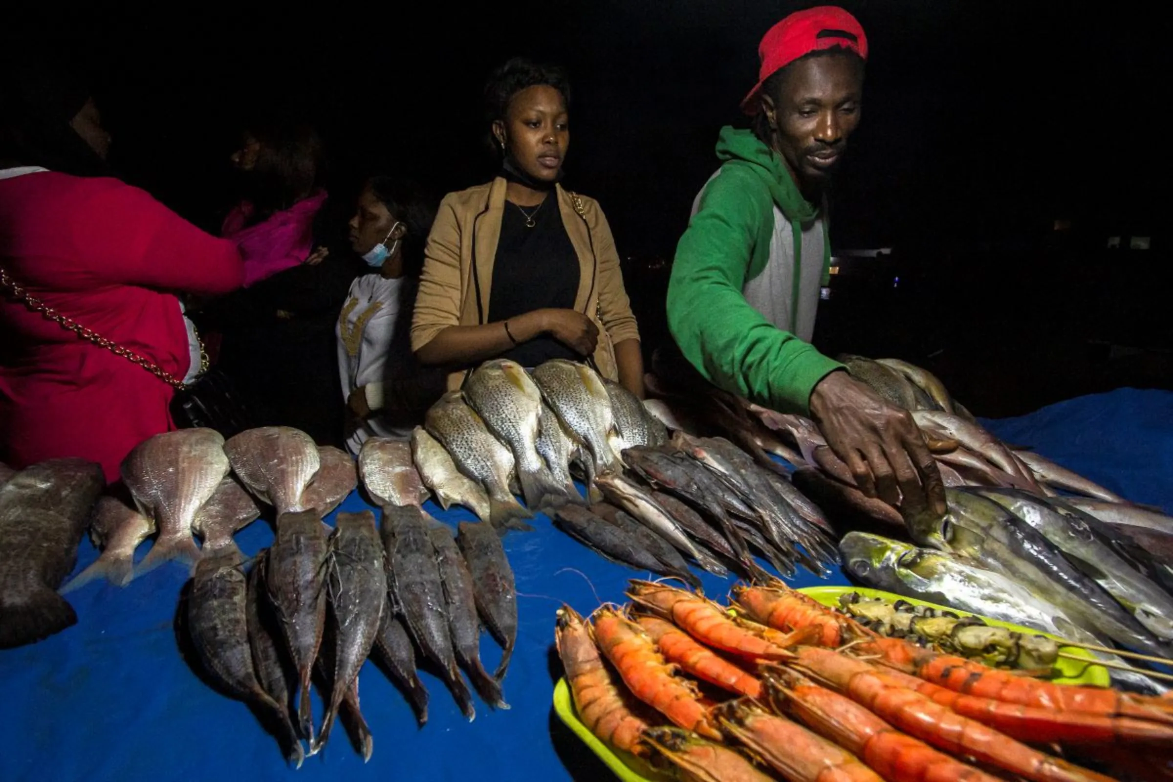 Fish vendor Mbaye reaches for a fish to serve a customer during a night market in Marché Soumbédioune, Dakar, Senegal, January 30, 2022. Marta Moreiras for StreetNet/Handout via Thomson Reuters Foundation