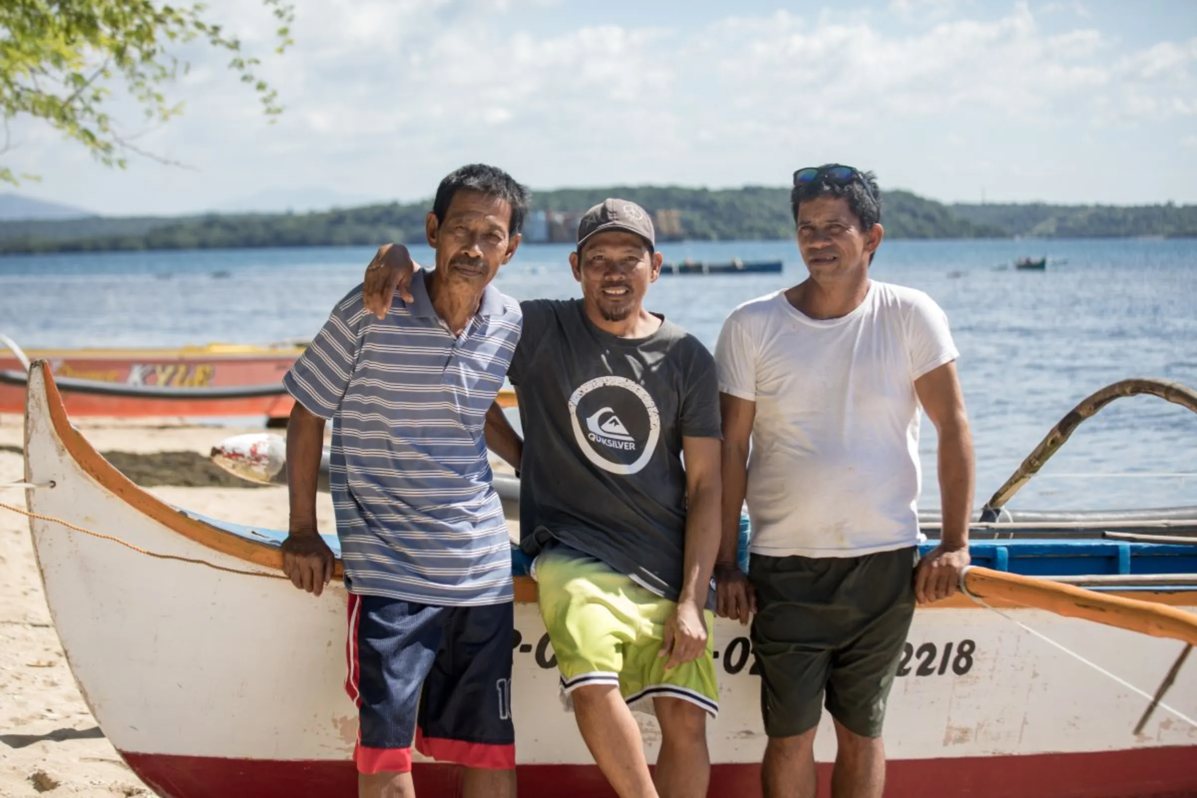Fishermen Rony Drio (L), Job Emata and Jimmy Tabat pose in front of a boat on a beach in San Salvador Island, Masinloc in Zambales Province in the Philippines. Fishermen on the island say China’s attempts to block them from fishing at the Scarborough Shoal is costing them money and threatening their livelihoods. Nov. 16, 2023. Thomson Reuters Foundation/Kathleen Limayo