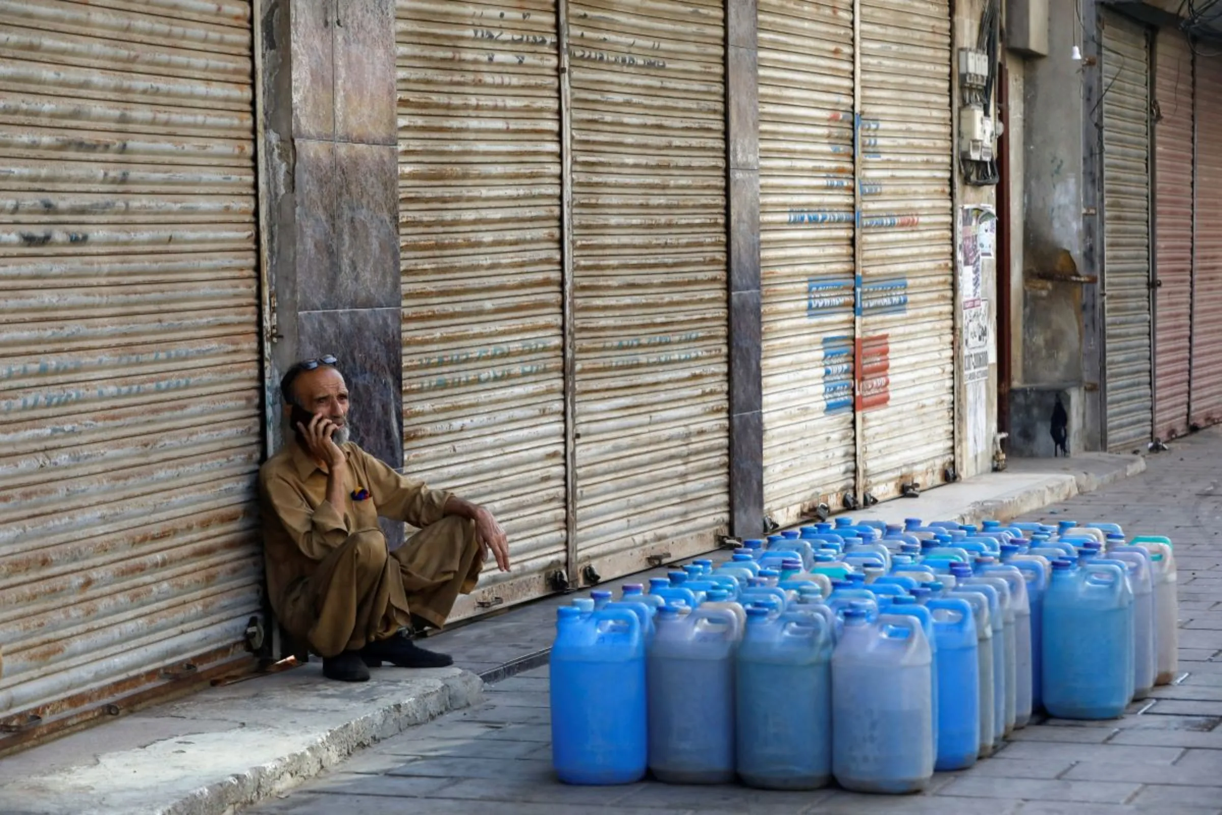 A shopkeeper uses mobile phone as he sits outside closed shops during a shutter down strike called by the Tehreek-e-Labbaik Pakistan (TLP), a religious and political party, against inflation and recent increase in prices of petroleum products in Karachi, Pakistan February 27, 2023. REUTERS/Akhtar Soomro