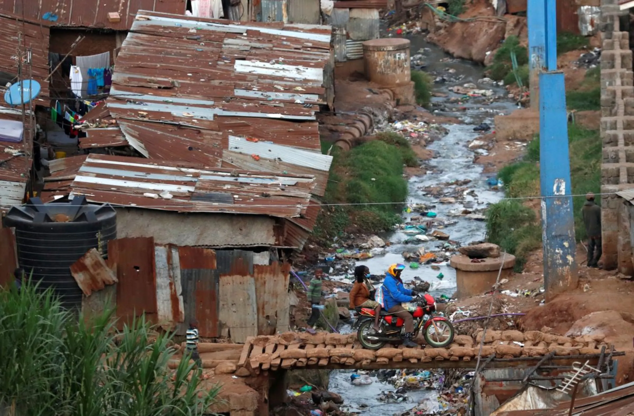 A rider and a passenger cross a wooden bridge over a polluted stream, within Kibera slums in Nairobi, Kenya July 6, 2020