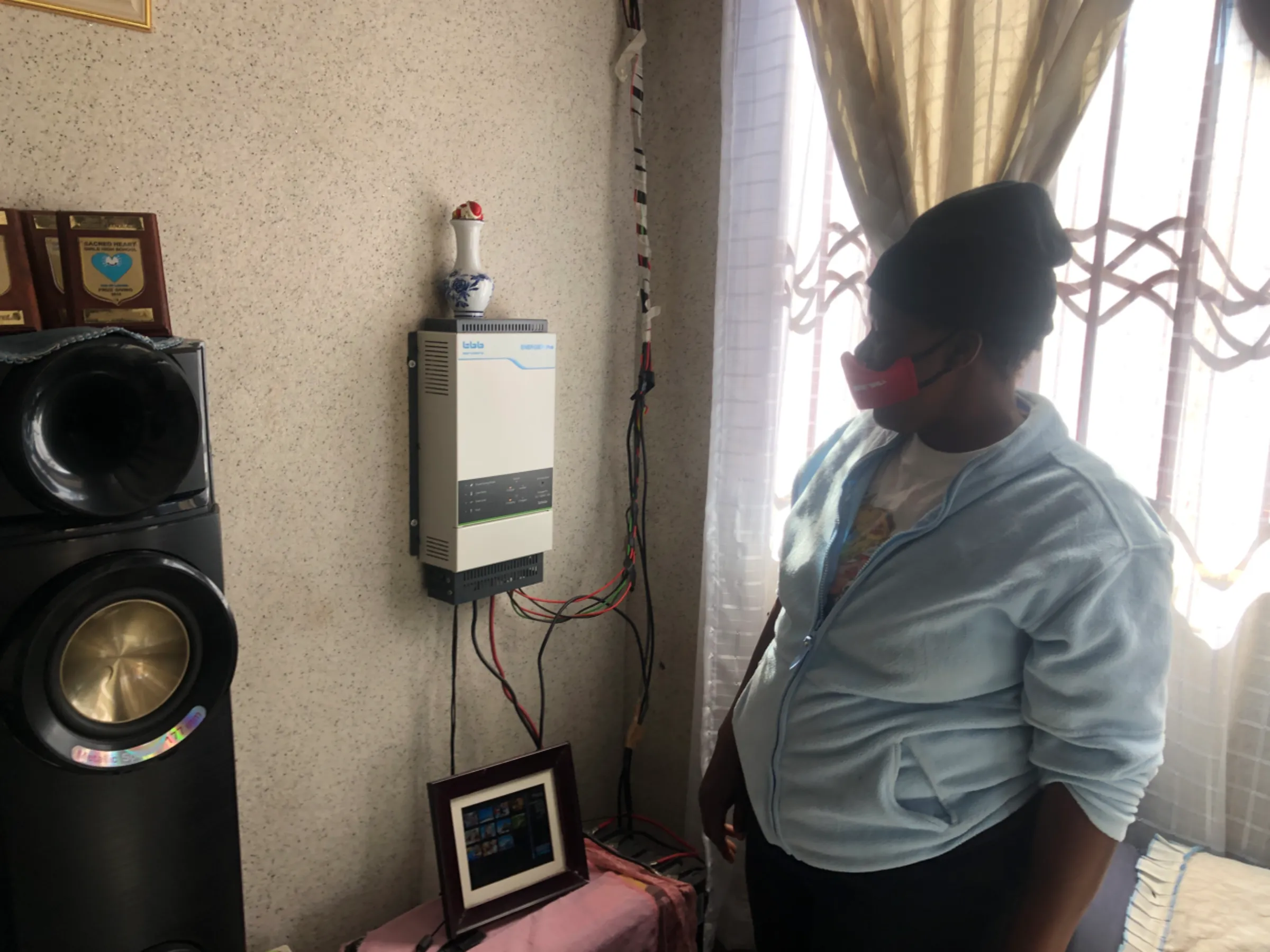 Buhle Siwela poses next to a solar inverter and solar batteries in her home, in the southern city of Bulawayo, Zimbabwe. July 9, 2022