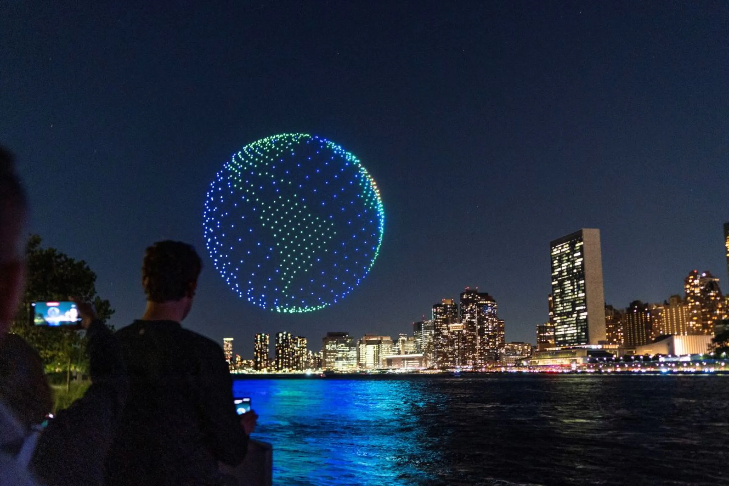 People watch drones creating a 3-D display outside the United Nations Headquarters calling attention to the Amazon rainforest and climate change in New York U.S., September 15, 2023. REUTERS/Eduardo Munoz