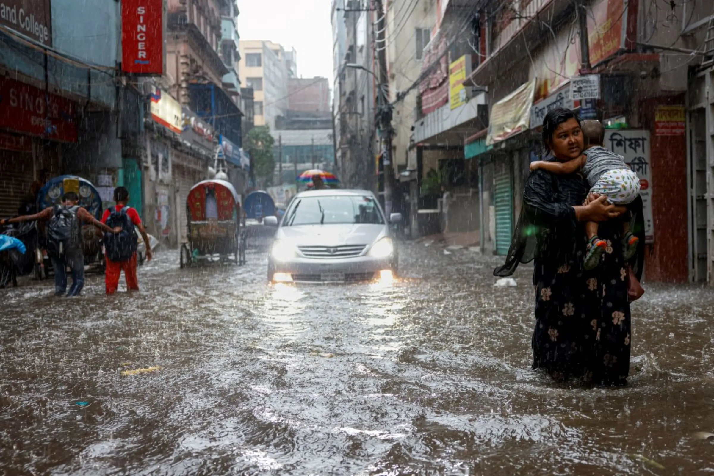 A woman carries a child while walking along a flooded street during heavy rain in Dhaka, Bangladesh, June 12, 2023. REUTERS/Mohammad Ponir Hossain