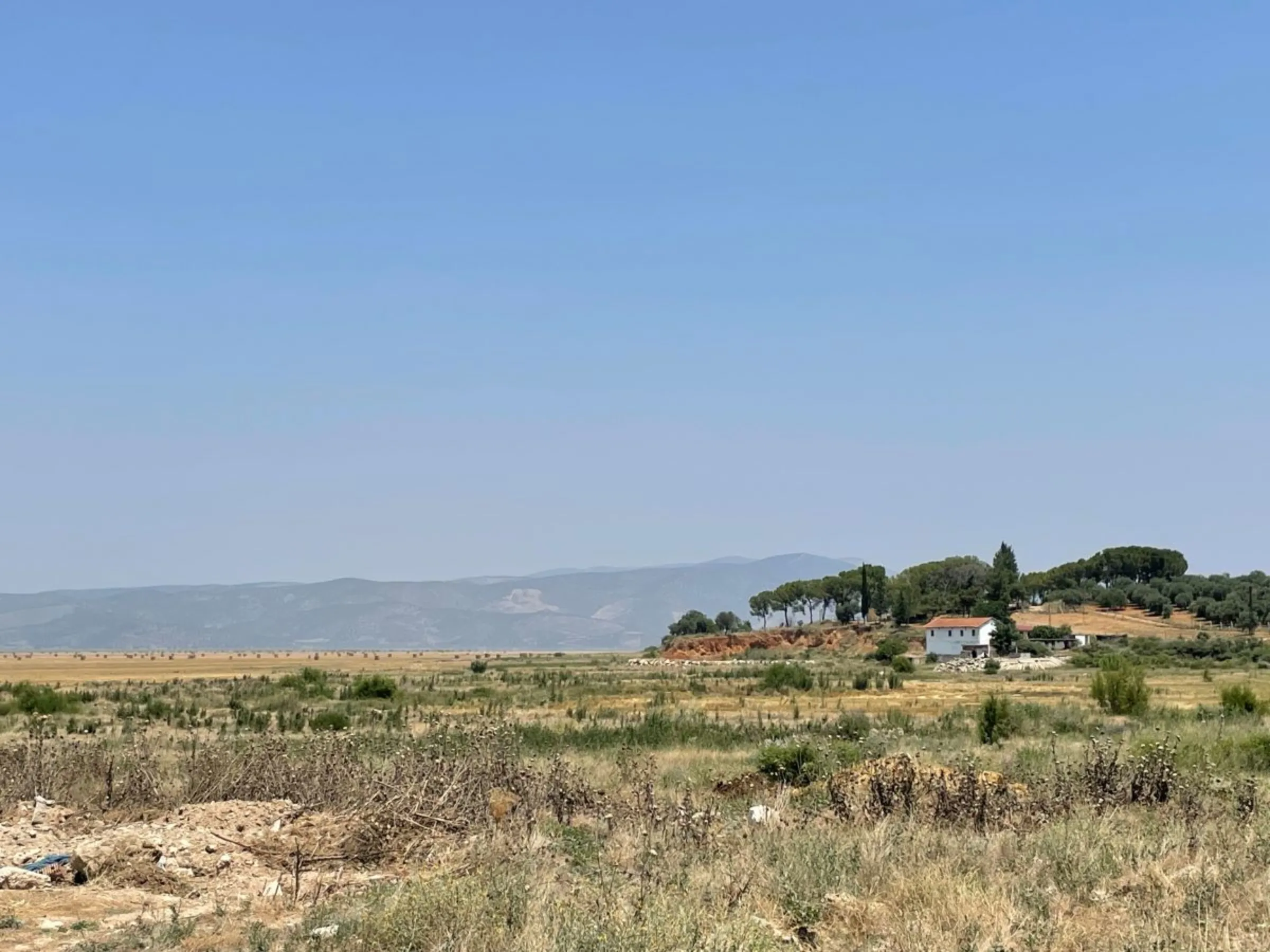 The fishermen’s cooperative building, which used to be at the water’s edge, now overlooks haybales in the dried-out basin of Lake Marmara, where agricultural work is beginning. Lake Marmara, Manisa, Turkey. July 13, 2023. Thomson Reuters Foundation/Beatrice Tridimas