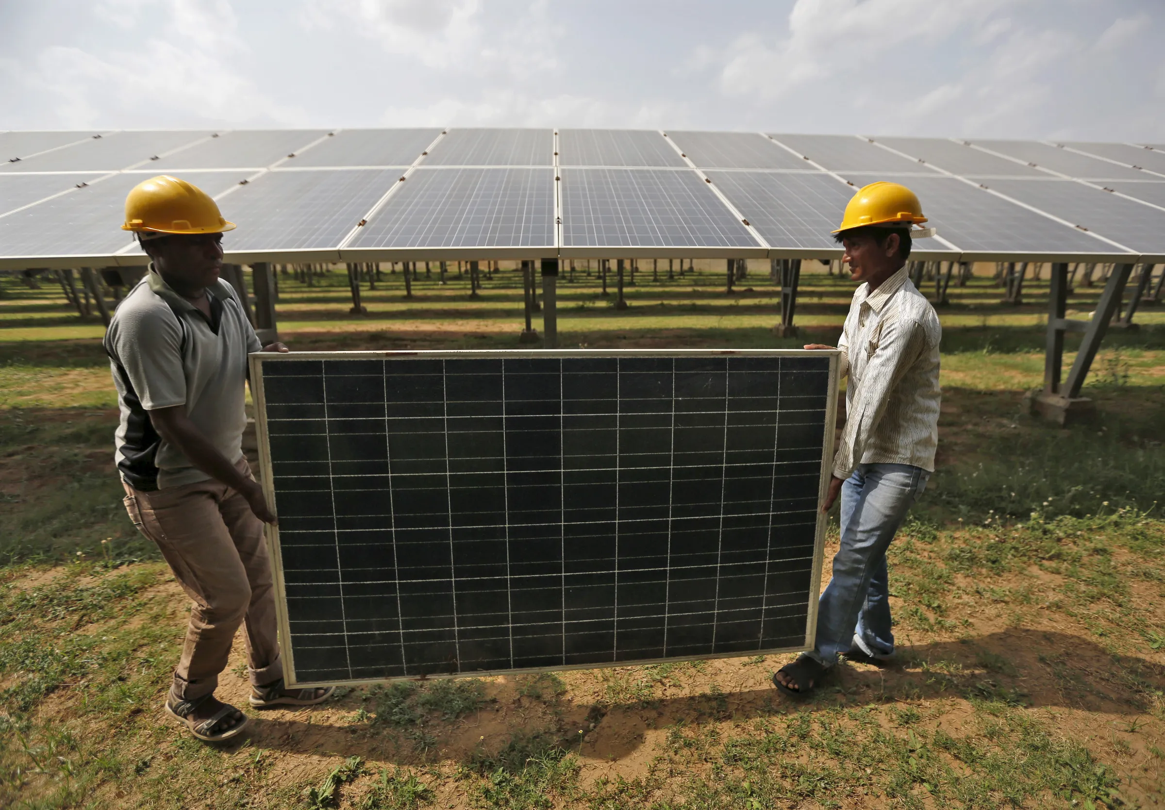 Workers carry a damaged photovoltaic panel inside a solar power plant in Gujarat,