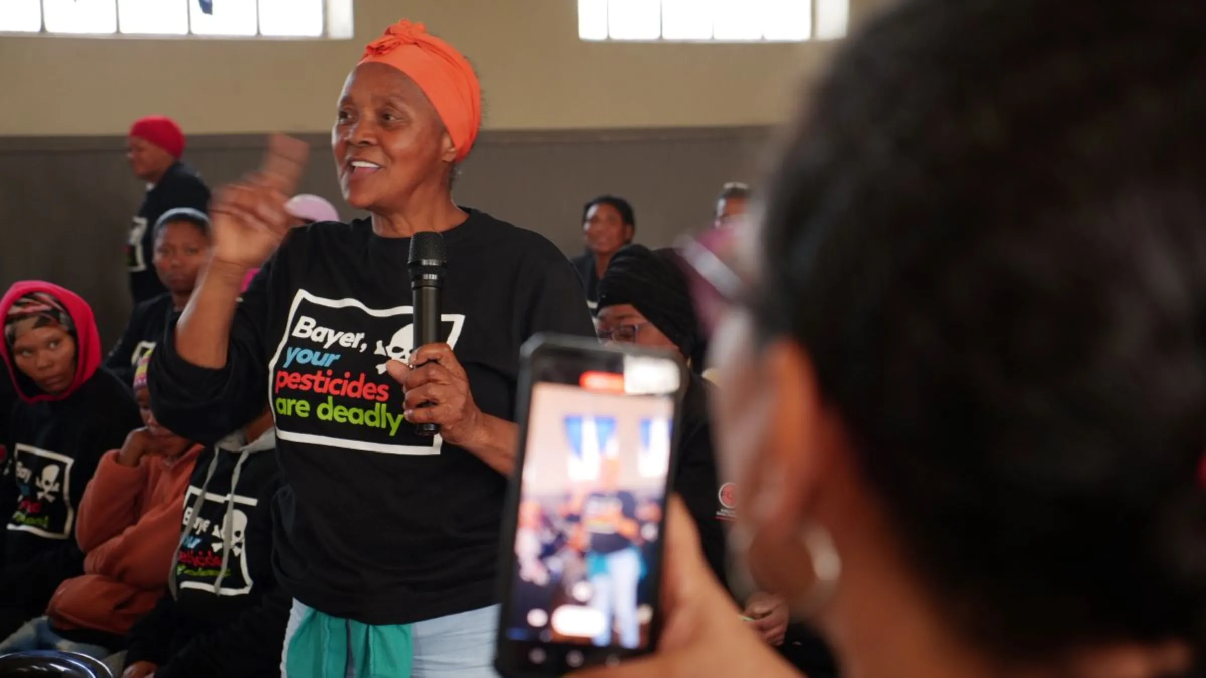 A female farmworker is filmed on a cellphone as she speaks into a microphone sharing stories of pesticide exposure in Paarl, South Africa, September 8, 2023. Thomson Reuters Foundation/Kim Harrisberg