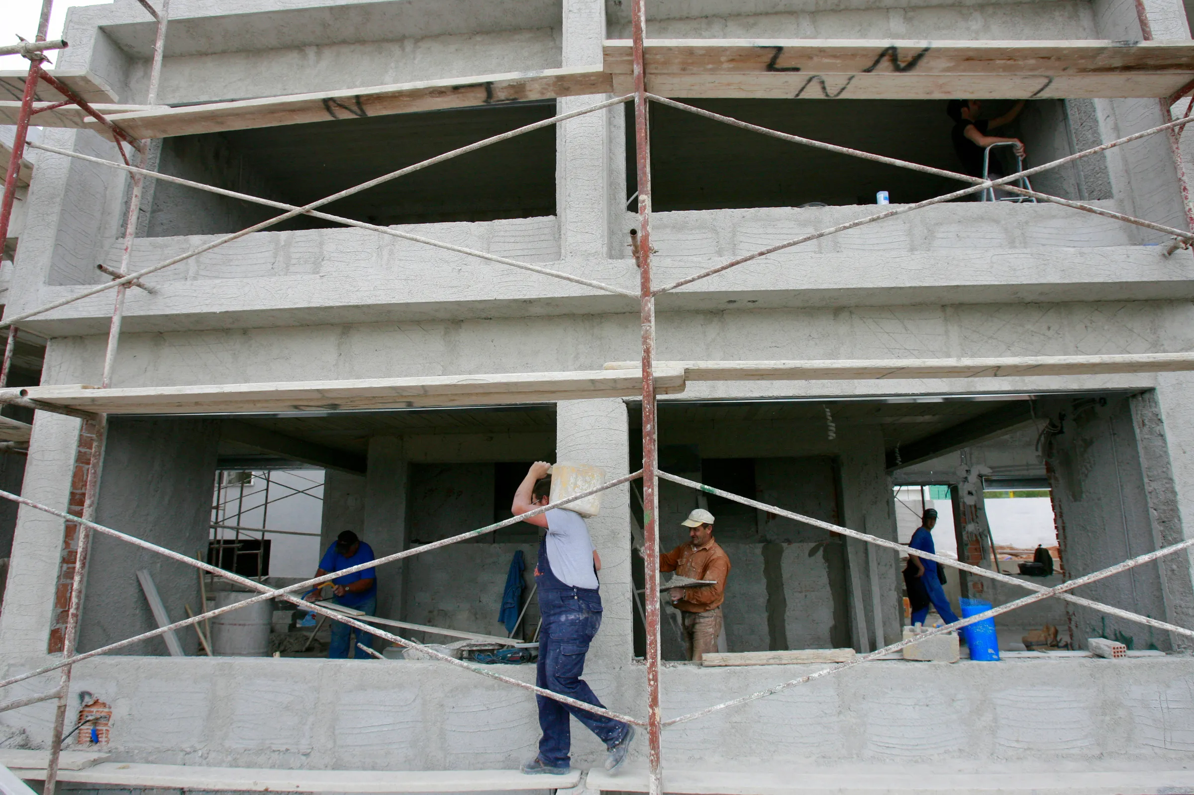 Scaffolding covers the front of a building shell while men work in the rooms