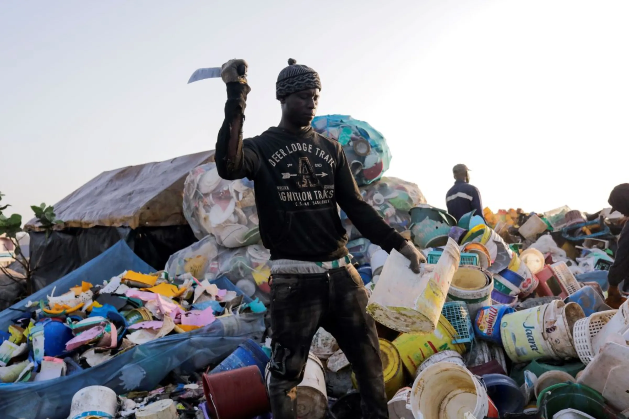 A man uses his machete to cut recyclable plastic buckets at the garbage dumping site in Senegal, April 29, 2022. REUTERS/Ngouda Dione