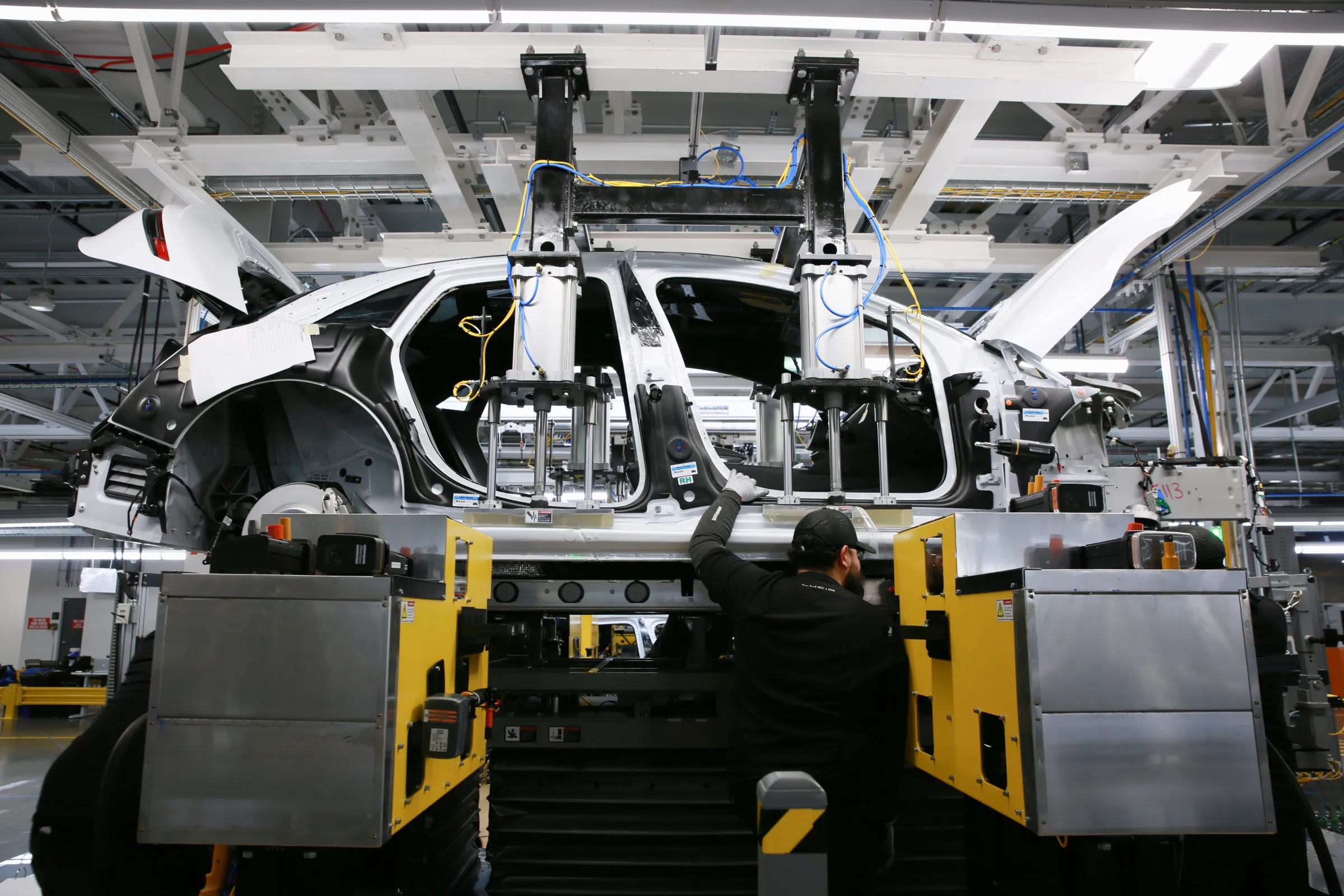 Workers marry the body structure with the battery pack and the front and rear sub frames as they assemble electric vehicles