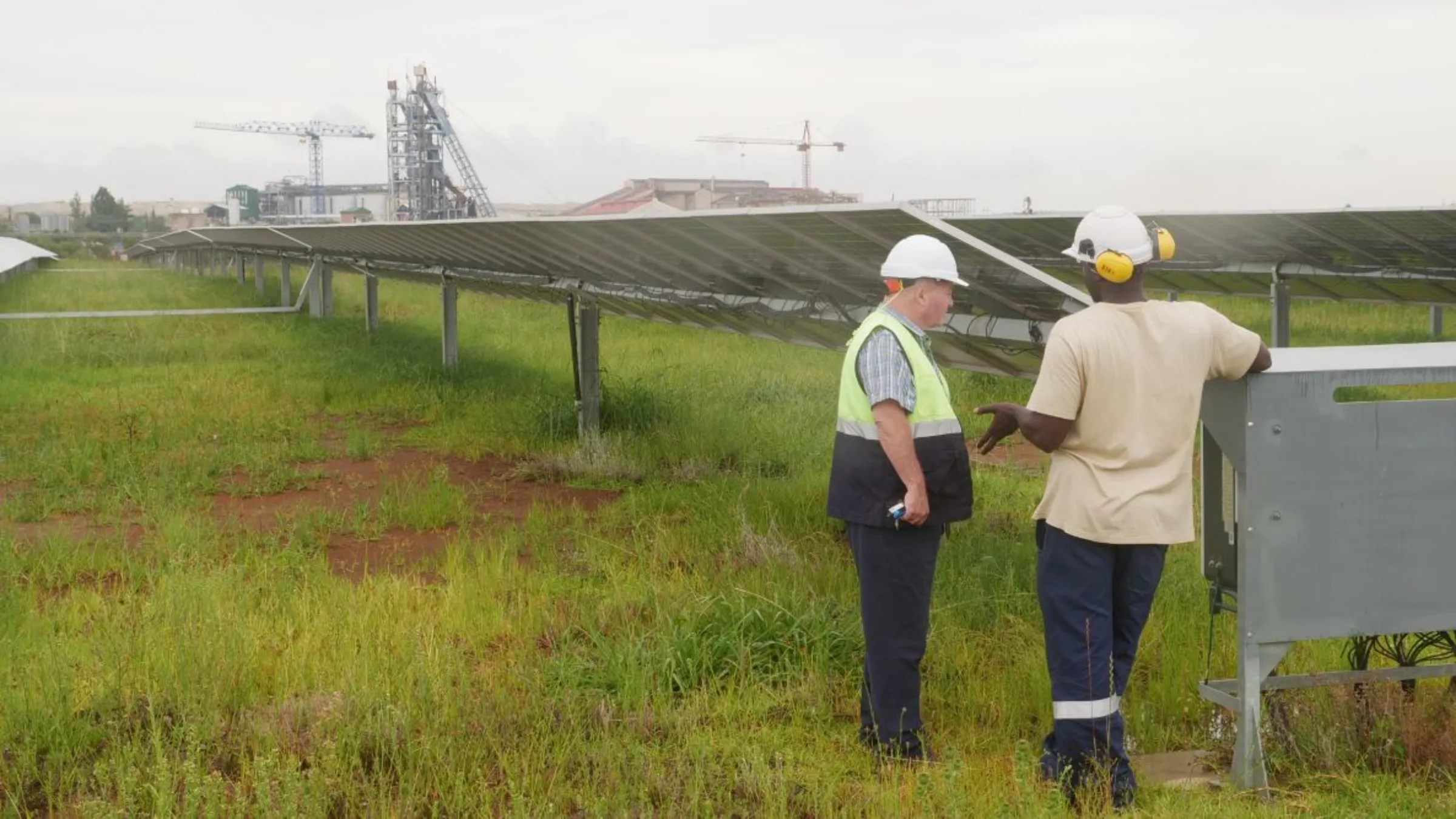 Two employees of the Pan African Resource’s gold mine talk in front of a solar farm used to power the gold mine in Mpumalanga, South Africa, February 1, 2023