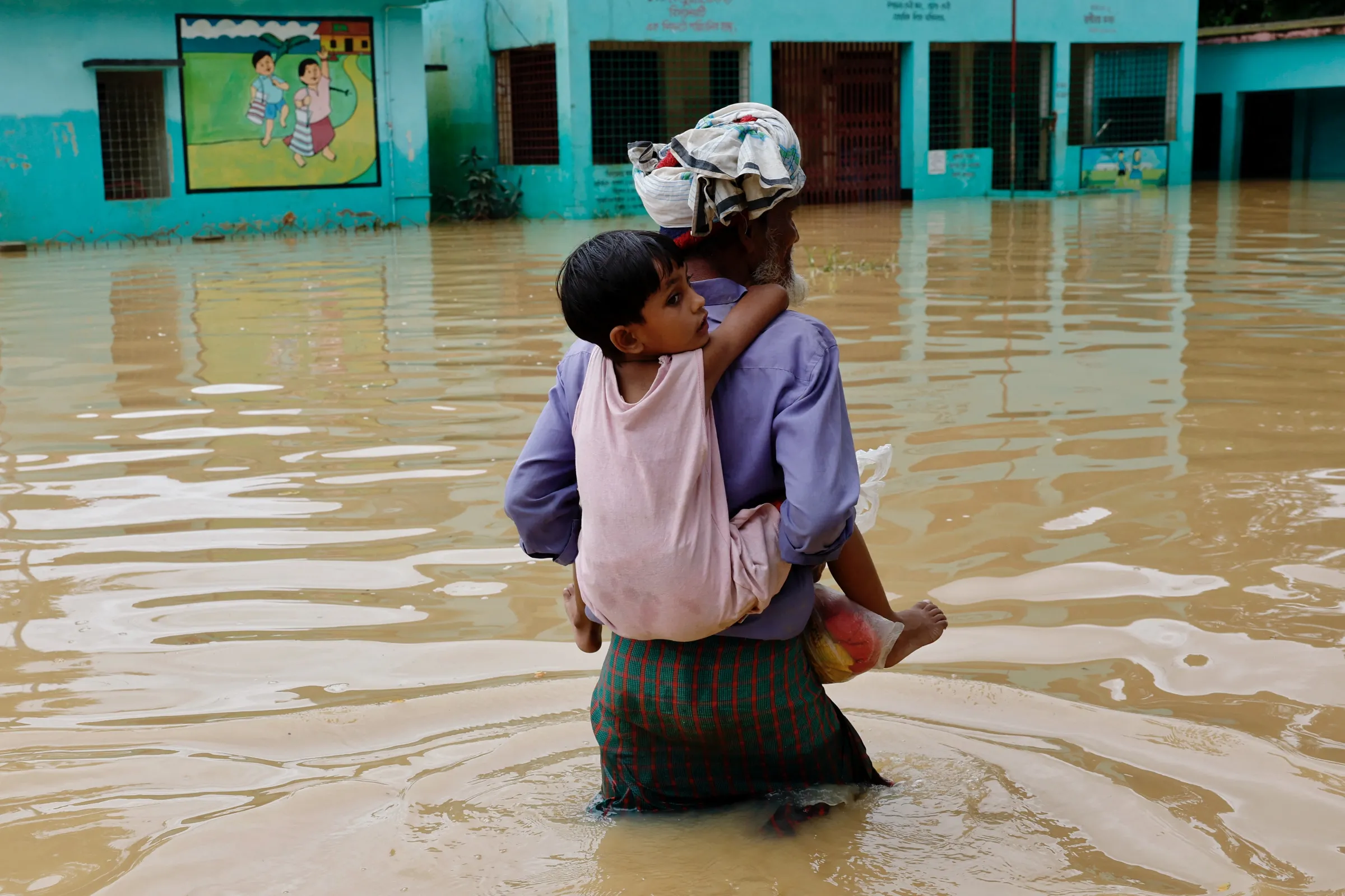 A man carries his granddaughter on his back while wading through flood water in the Fazilpur area of Feni, Bangladesh, August 26, 2024. REUTERS/Mohammad Ponir Hossain