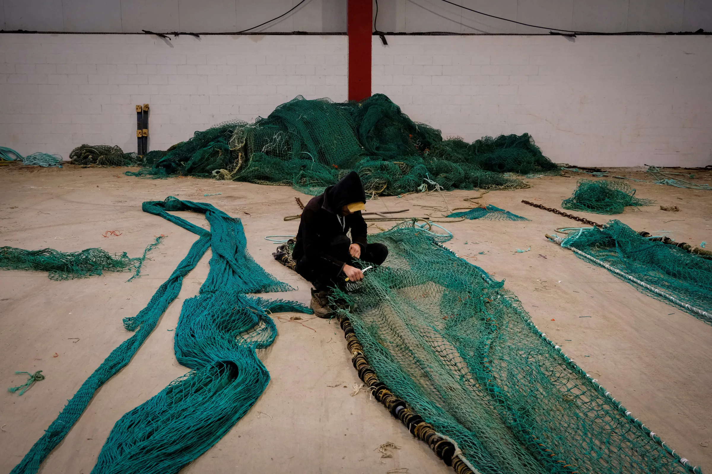 A man cuts and sews nets authorized to operate at depths on trawlers in Galicia, Spain, December 1, 2023. REUTERS/Nacho Doce