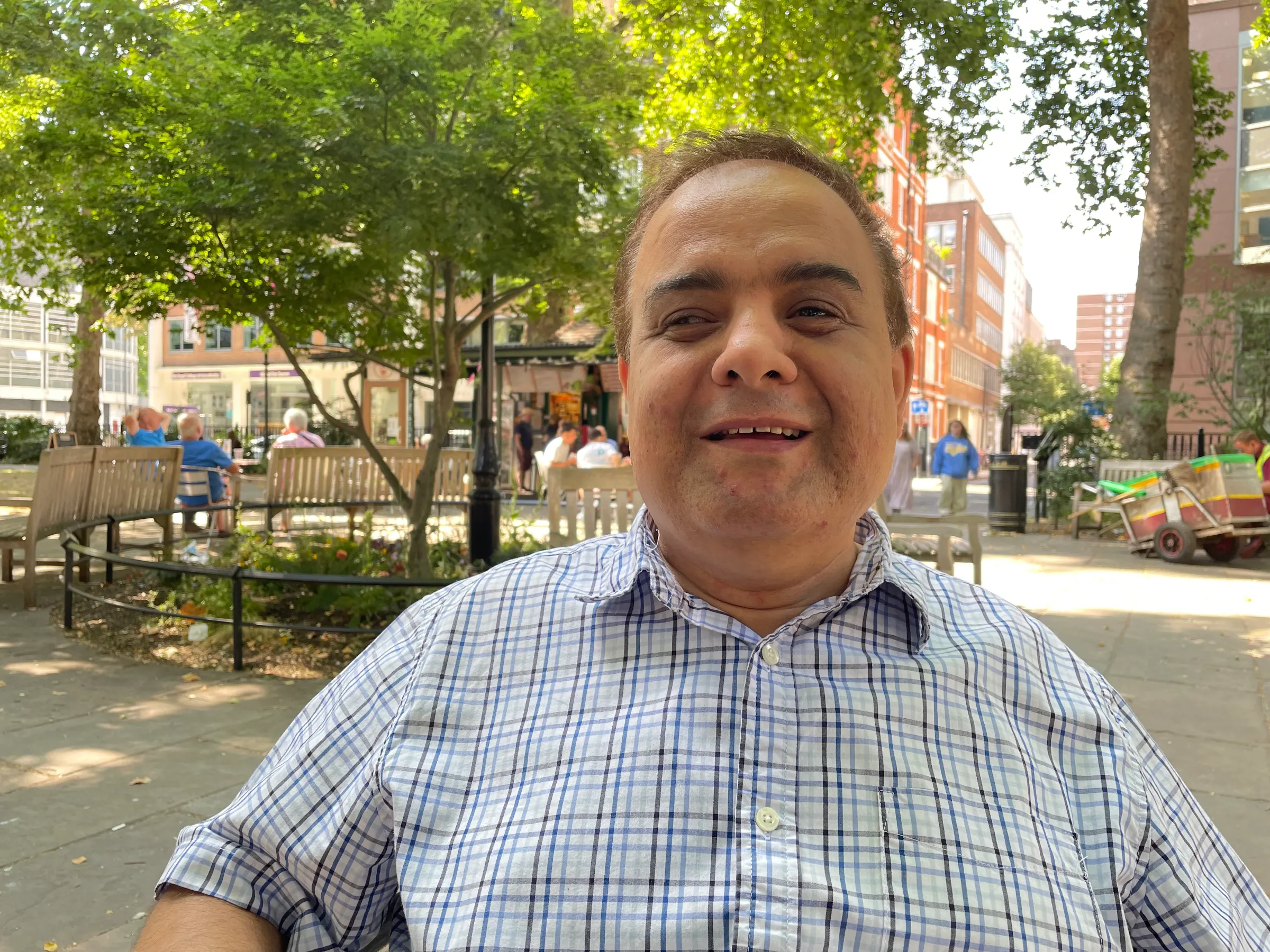 A man smiles as he is sat in a park