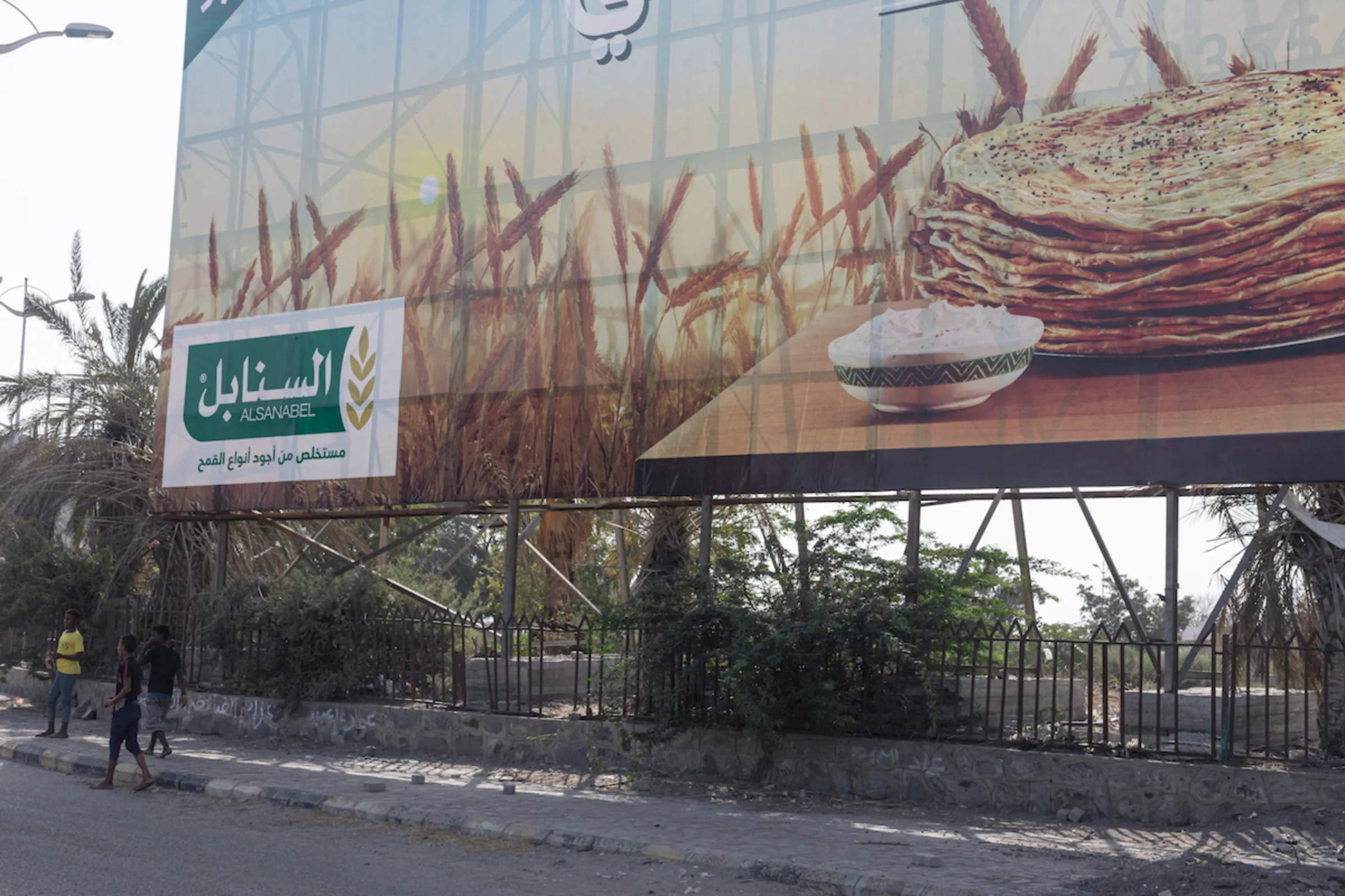 Men stand beneath a billboard advertising wheat flour, in Aden, Yemen, on February 21, 2022. Thomson Reuters Foundation/Sam Tarling