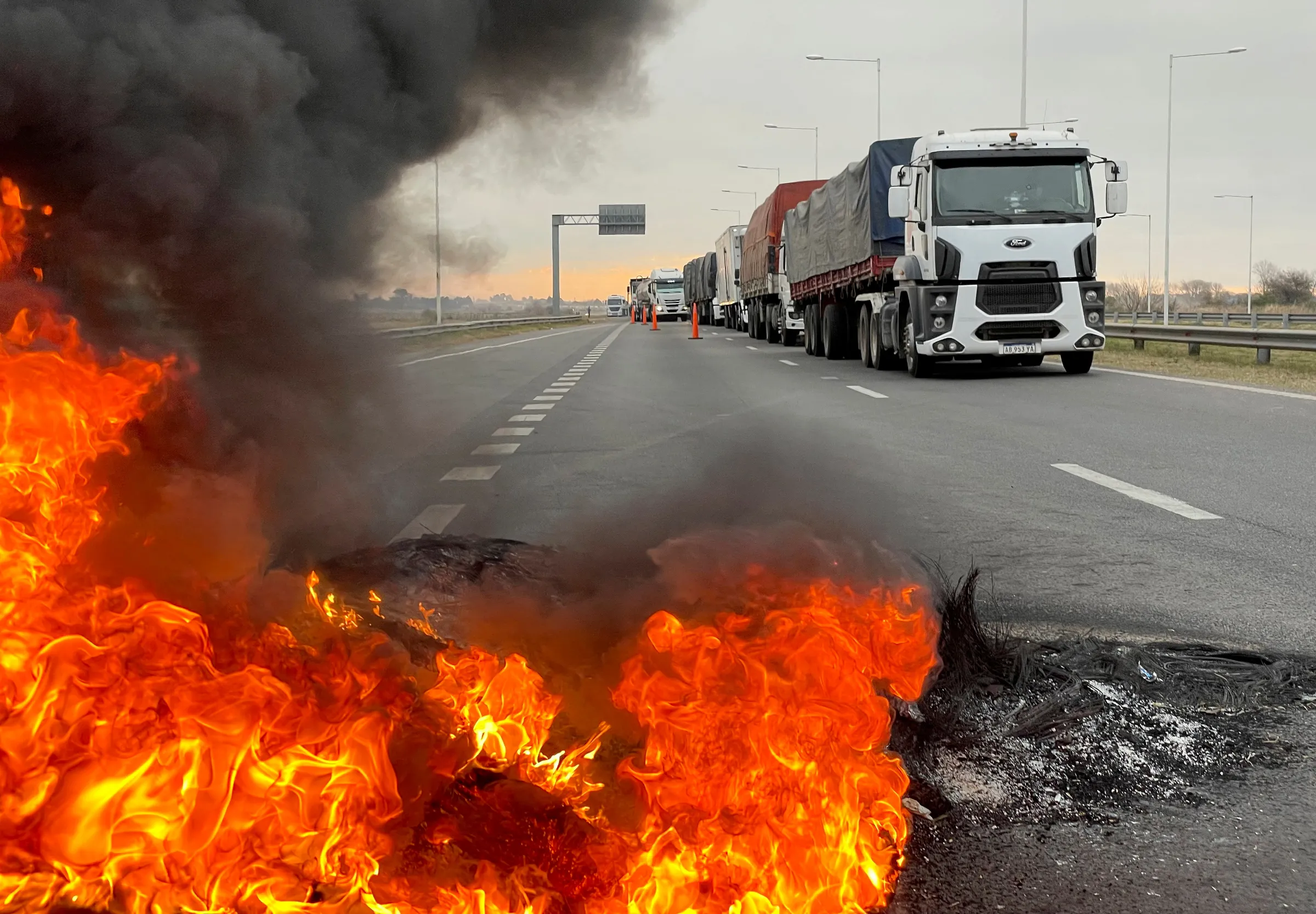 Trucks blocking a highway are pictured near a burning barricade as Argentine truck drivers protest against shortages and rising prices for diesel fuel, just as the country's crucial grains harvest requires transport amid surging inflation, in San Nicolas, Argentina June 23, 2022. REUTERS/Miguel Lo Bianco