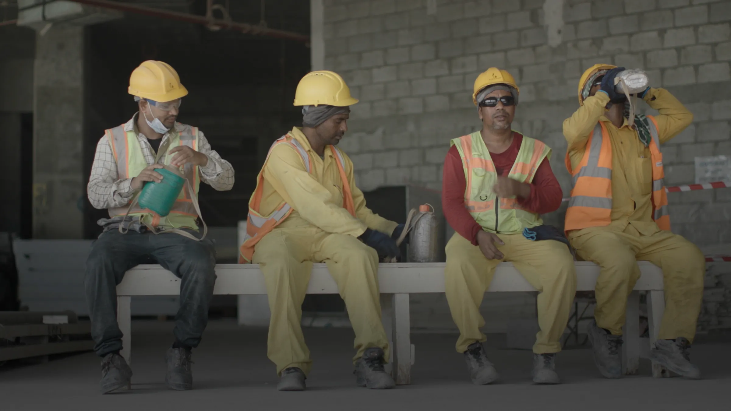 Four construction workers dressed in helmets sit on a bench