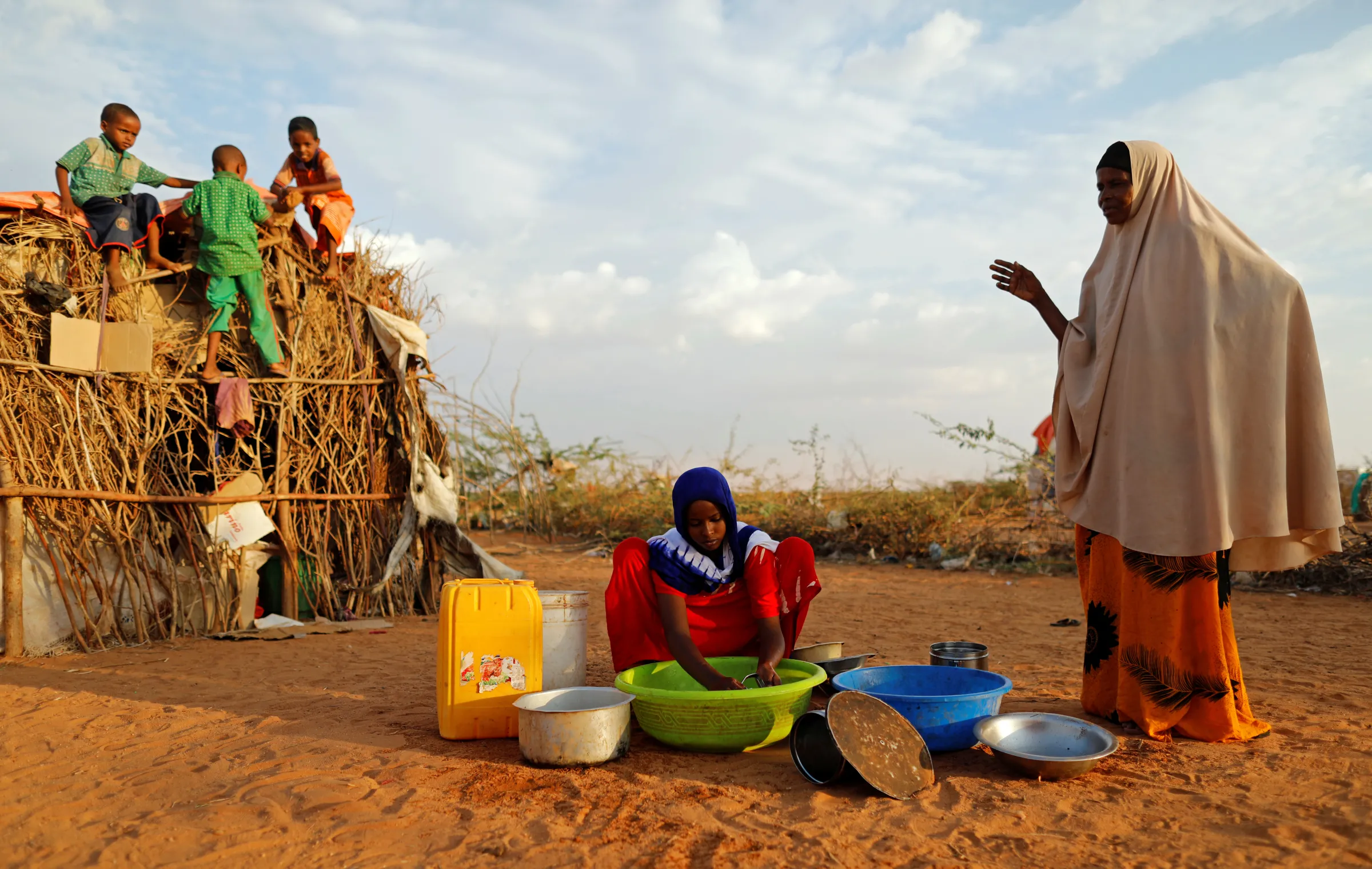 A girl washes dishes as her mother gestures and her nephews play at a camp for internally displaced people from drought hit areas in Dollow, Somalia April 3, 2017