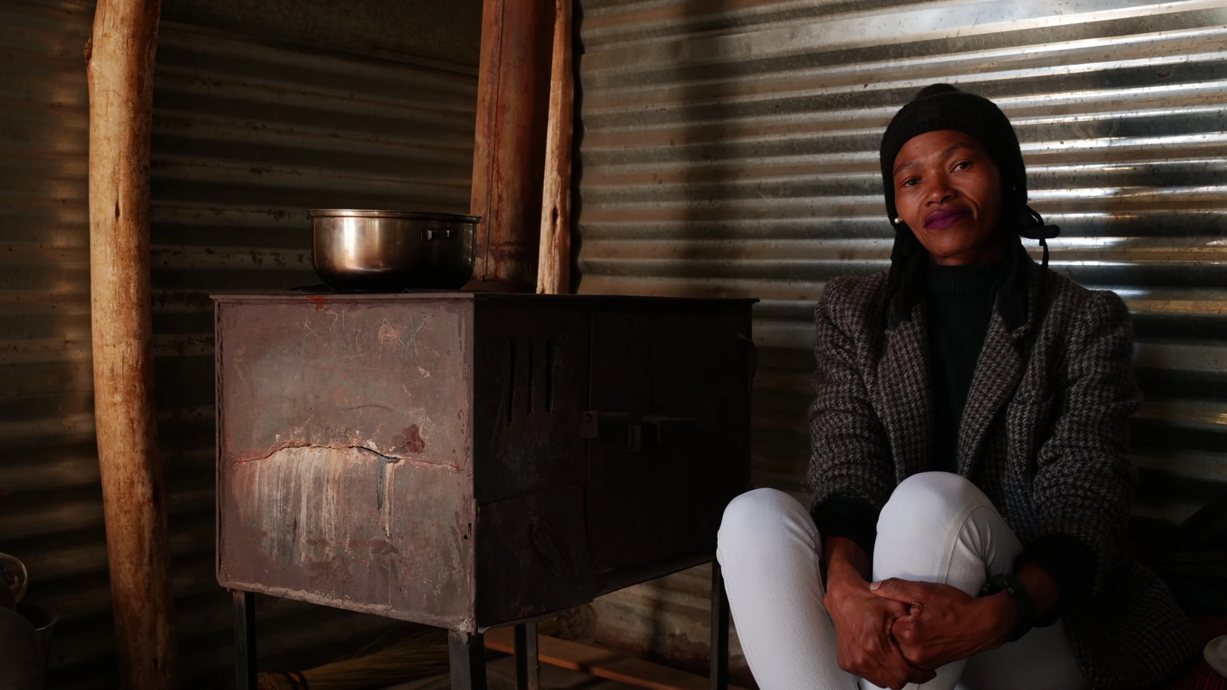 Nelly Nkosi, women's officer with the Khuthala Environmental Care Group, sits alongside her coal stove used for cooking and heating in her home in Nomzamo, South Africa, July 10, 2025. Thomson Reuters Foundation/Kim Harrisberg