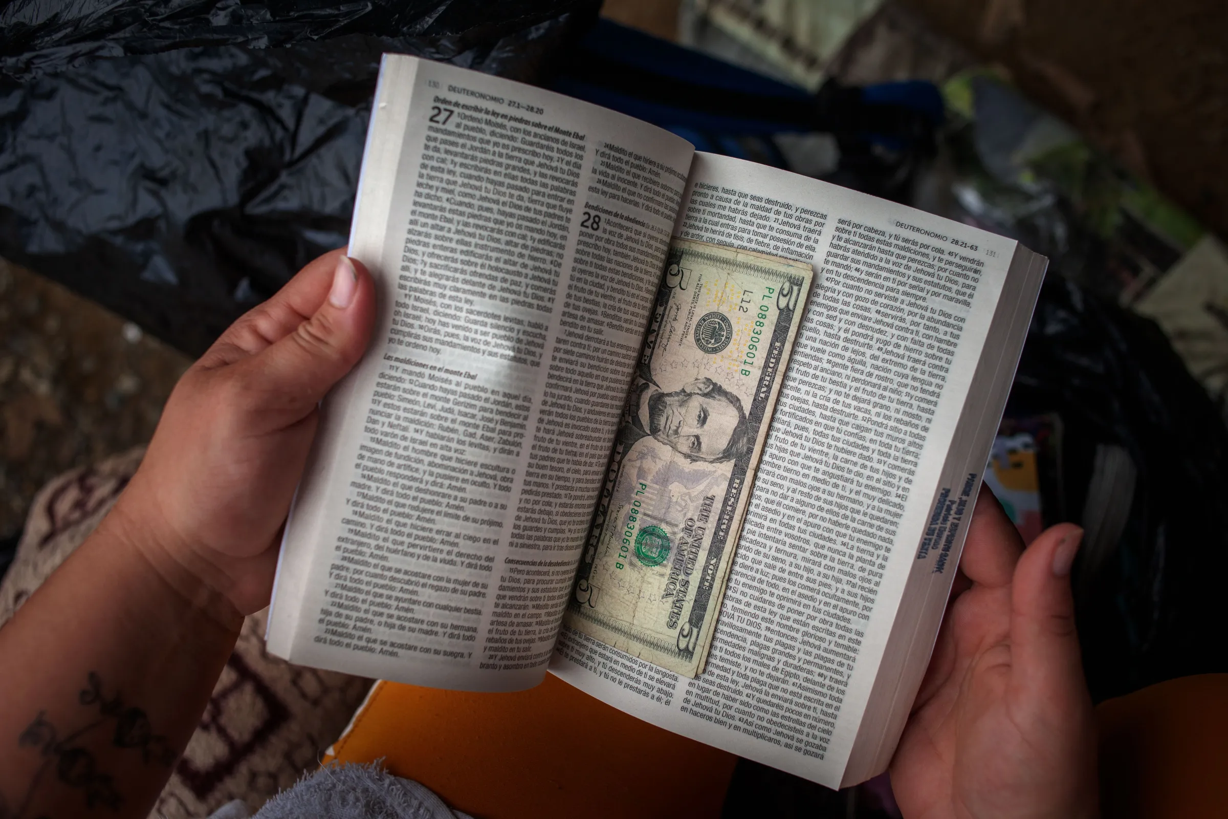 A Venezuelan migrant hides dollar bills in a bible carried in her backpack before negotiating a fee with jungle guides to take her and her family through the Darién  Gap at a camping site in the Colombian town of Capurganá where migrants gather before setting off on the jungle trek. Migrants pay about $160 each to be led through the Darién Gap to reach Panama. Capurganá, Colombia, July 27, 2022. Thomson Reuters Foundation/Fabio Cuttica