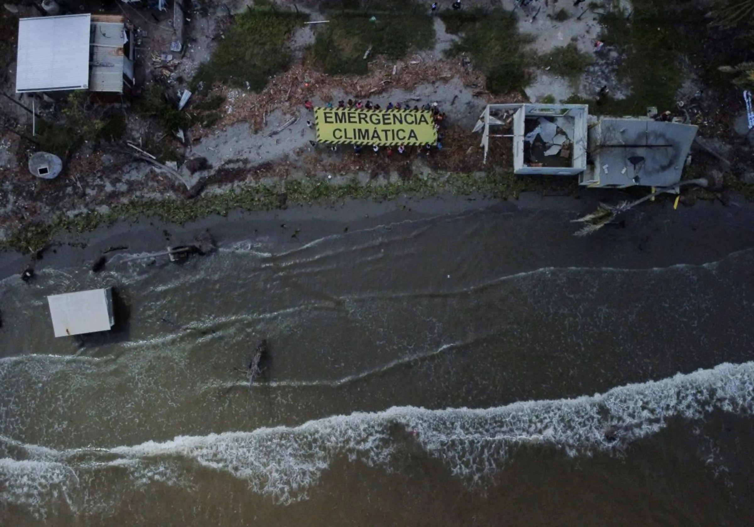 Activists and residents hold a banner reading 'Climate emergency' while standing near houses destroyed by rising sea levels, forcing villagers to relocate, in El Bosque, Mexico November 7, 2022. REUTERS/Gustavo Graf