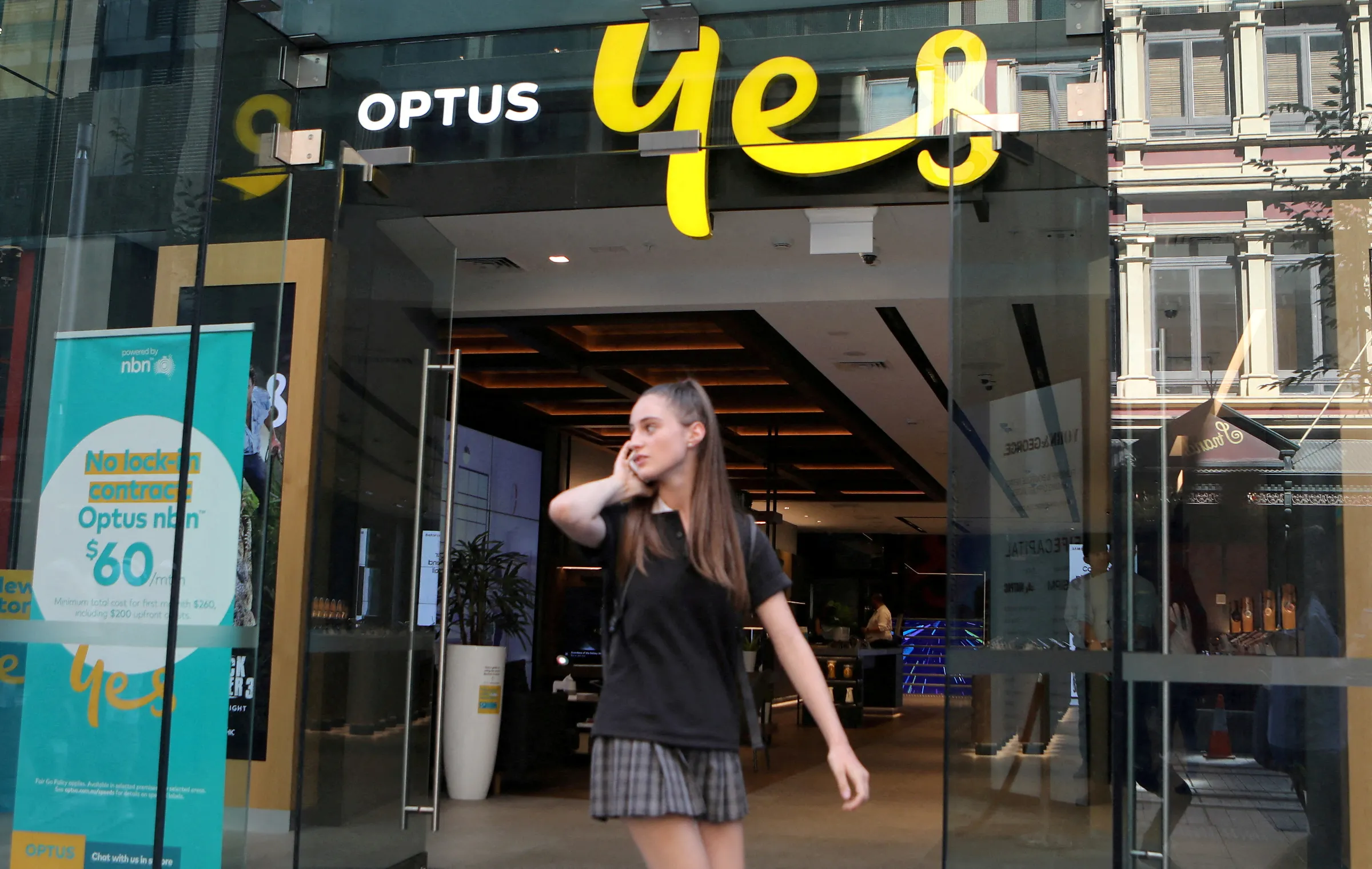 A woman uses her mobile phone as she walks past in front of an Optus shop in Sydney, Australia, February 8, 2018
