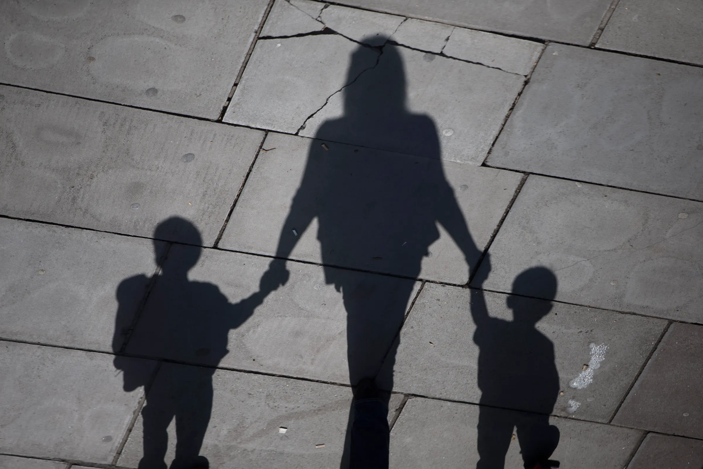 A woman and children cast their shadows as they stroll in the sunshine on the Southbank in London