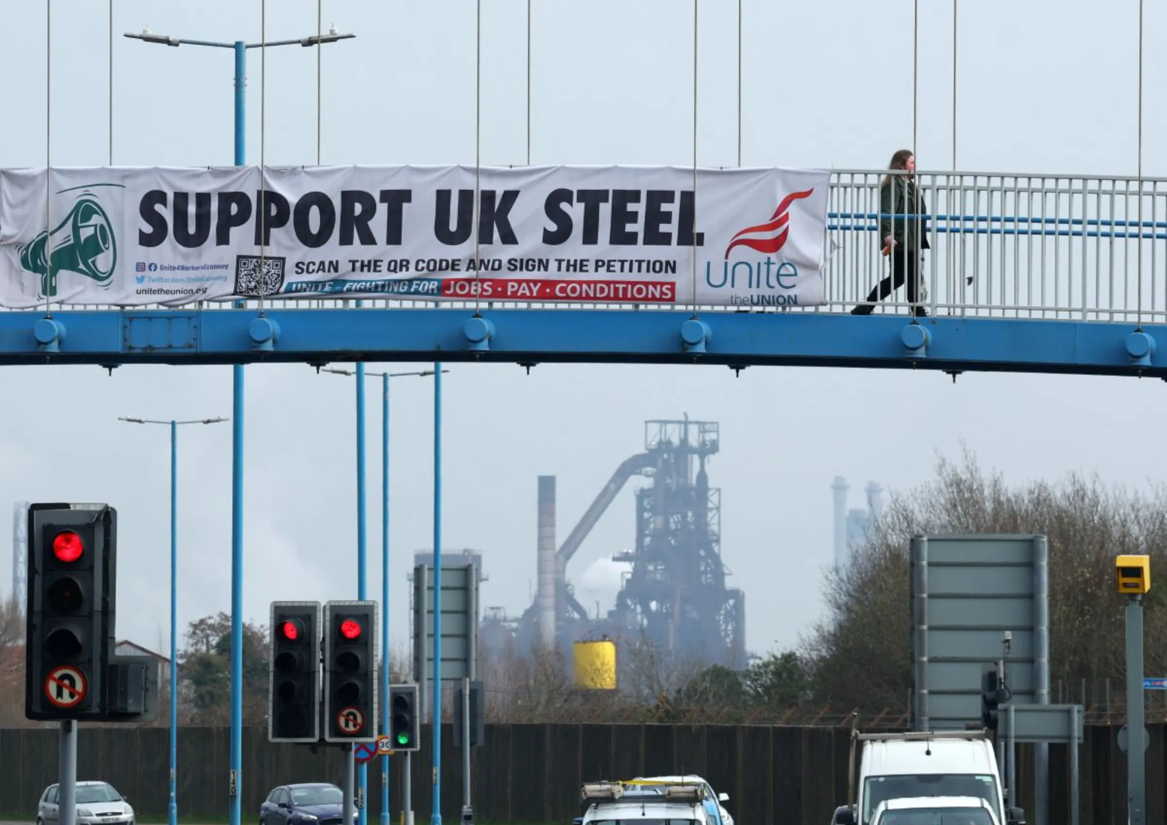 A person crosses a footbridge with Tata Steel Port Talbot steel production plant seen behind, ahead of its planned transition from blast furnace to electric arc furnaces, at Port Talbot, Wales, Britain, March 11, 2024. REUTERS/Toby Melville