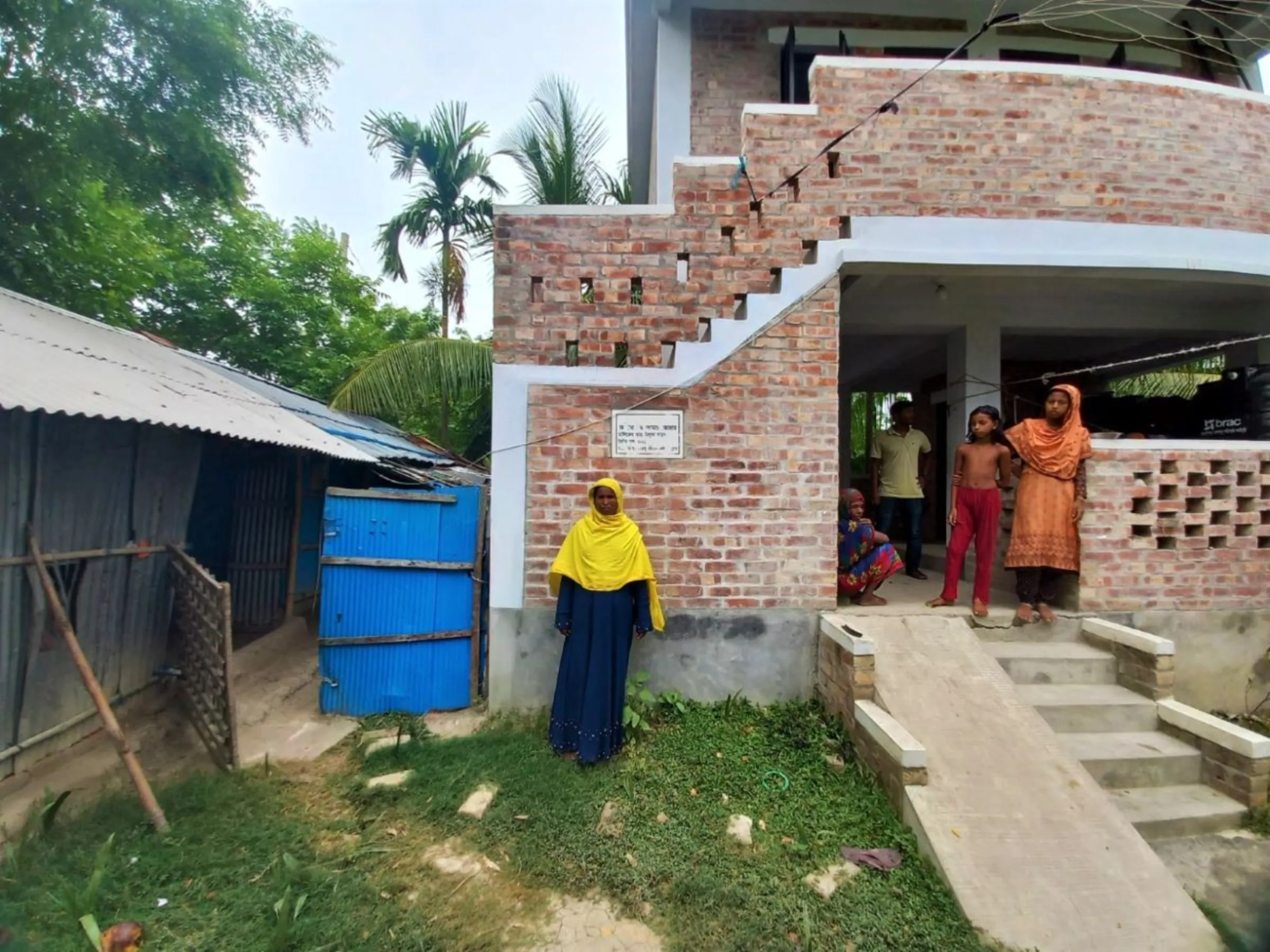 Nilufa Khatun and her family pose before the brick house that protects them from the periodic cyclones that hit the southern coast of Bangladesh once in every few years, June 8, 2023