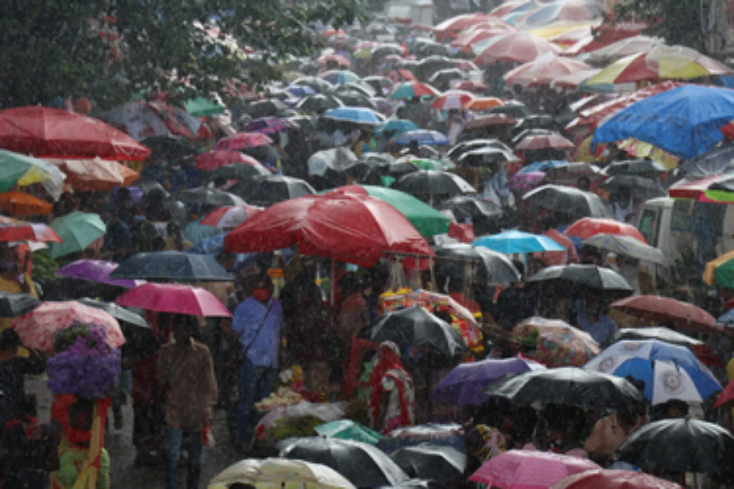 Shoppers take shelter under umbrellas during a rain shower at a crowded marketplace in Mumbai, India, September 9, 2021. Thomson Reuters Foundation/Niharika Kulkarni