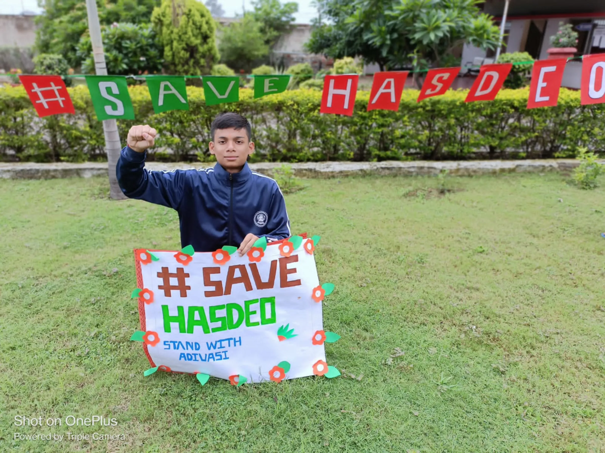 A student wearing uniform kneels with his fist in the air holding a climate poster