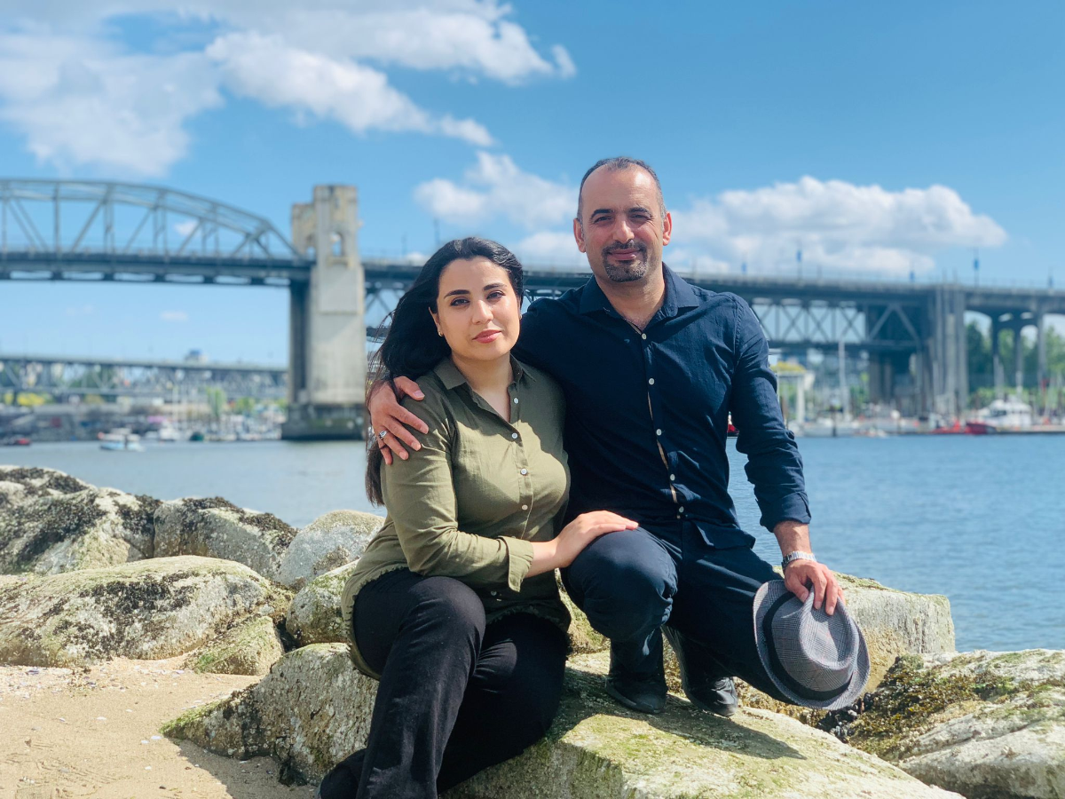 A man and woman pose for a photo while sat on rocks in next to a river in Vancouver