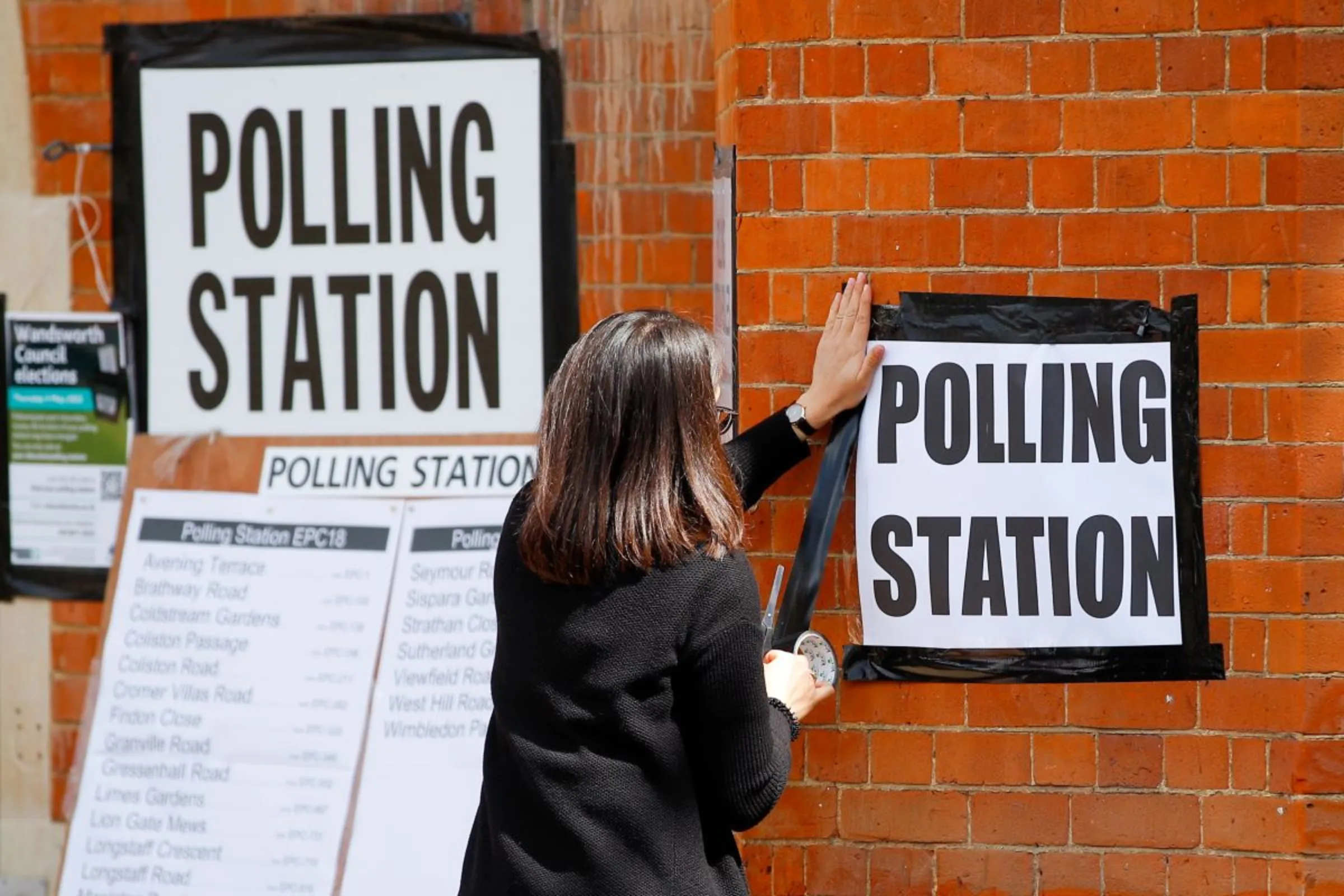 A woman attaches a sign on the wall of a polling station, during the local elections in London, Britain May 5, 2022