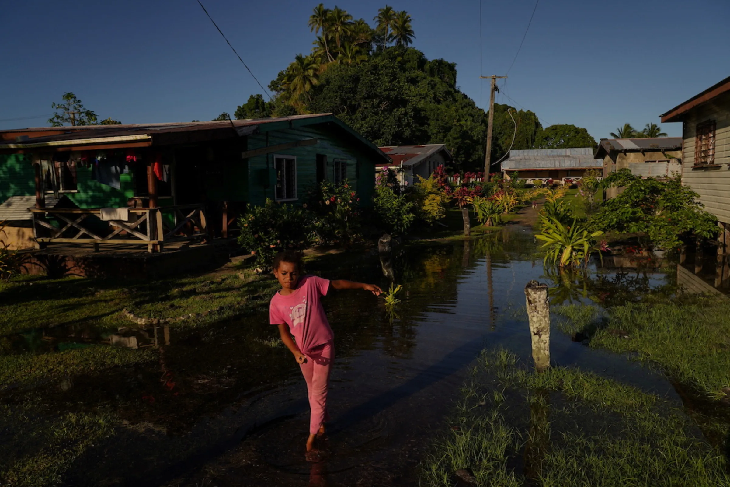 A local girl wades through seawater flooding her community during high tide in Serua Village, Fiji, July 15, 2022. As the community runs out of ways to adapt to the rising Pacific Ocean, the 80 villagers face the painful decision whether to move. REUTERS/Loren Elliott