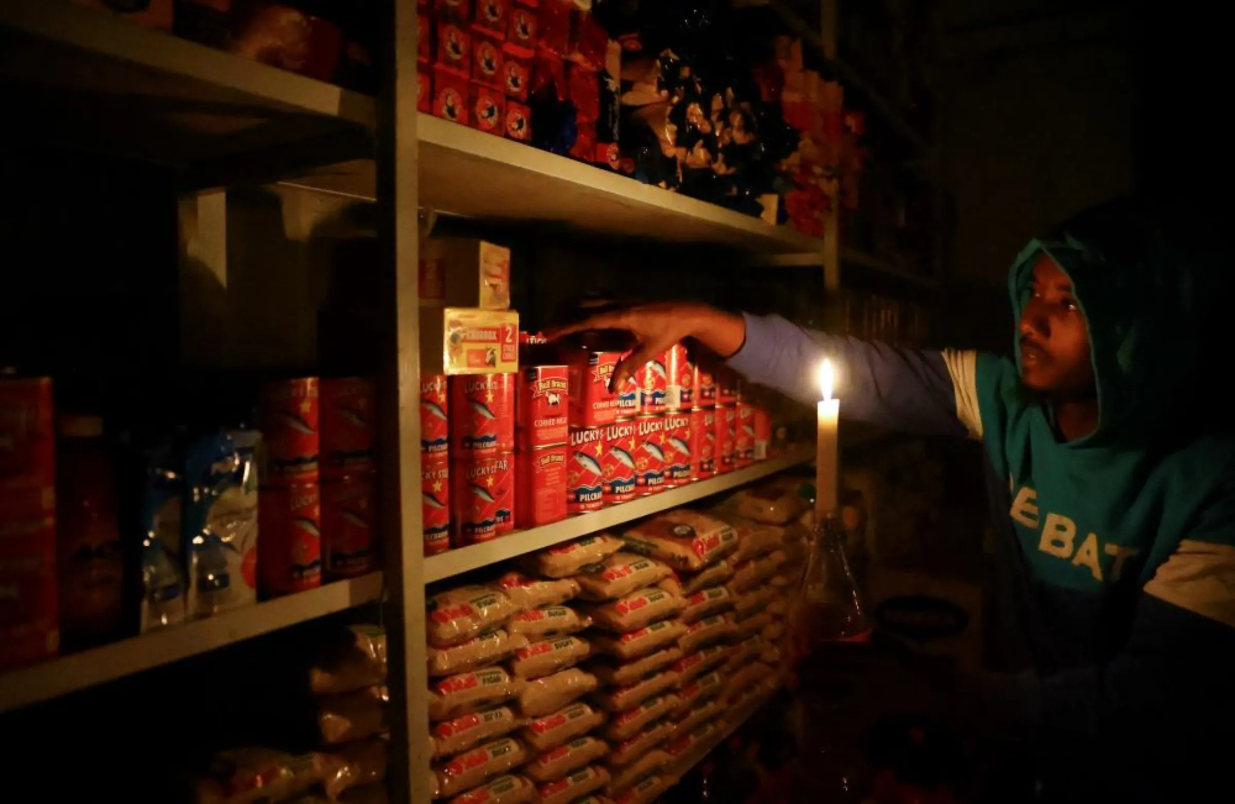 A shop owner picks an item for a customer by candlelight during power outages by South African utility Eskom due to more breakdowns at its ageing coal-fired plants, in Soweto, South Africa, April 20, 2022. REUTERS/Siphiwe Sibeko